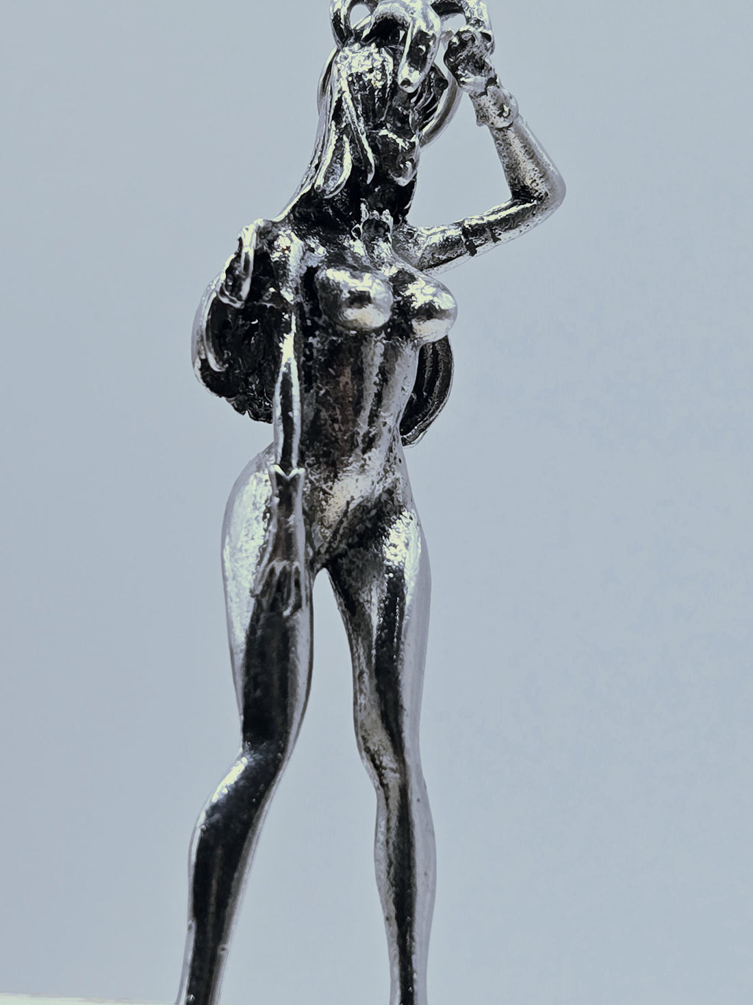 A silver-colored metal pendant in the shape of a female figure, with a wing-like design on her back and a detailed, sculpted appearance.