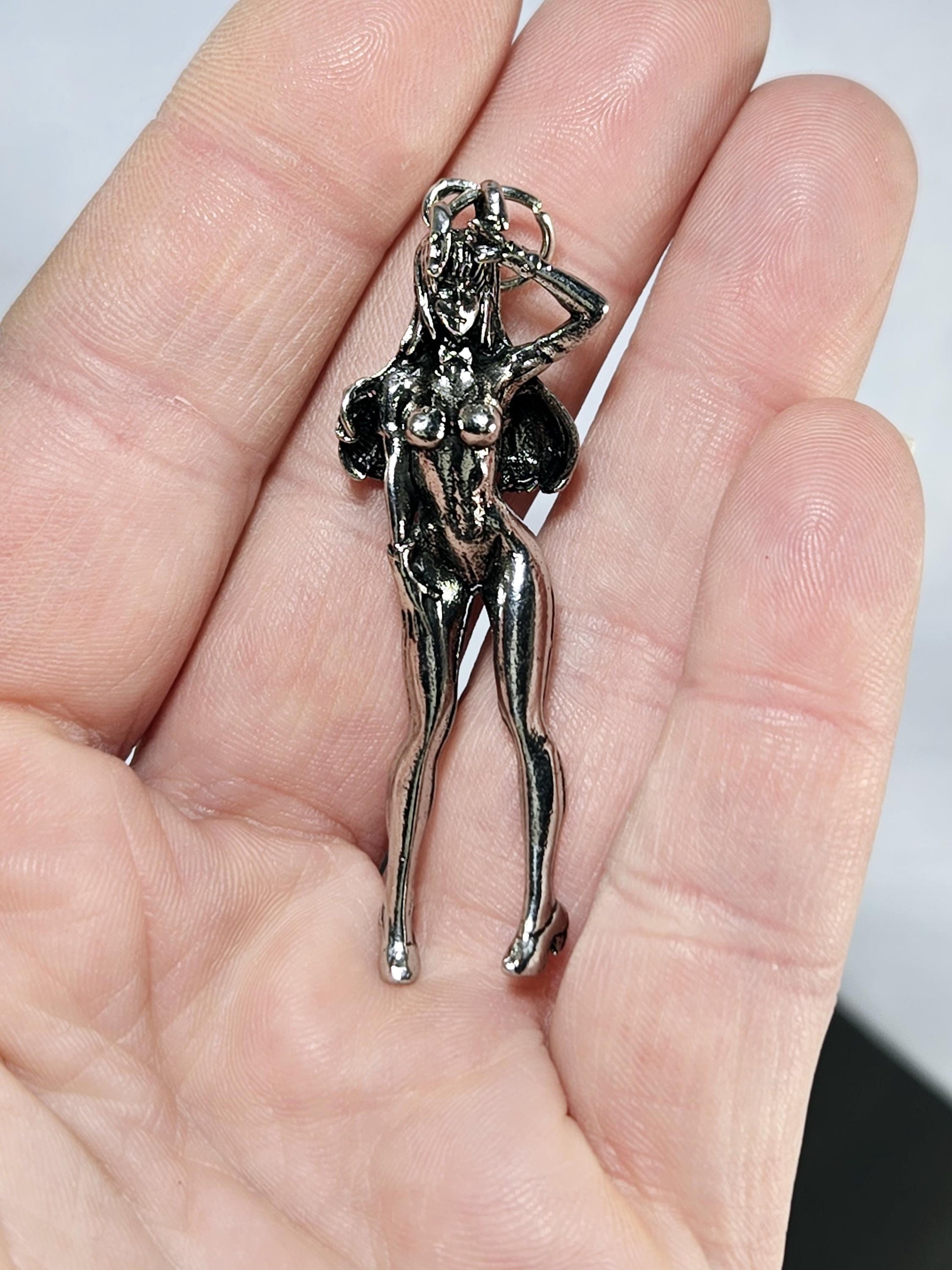 A hand holding a small silver-colored metal charm or pendant.
