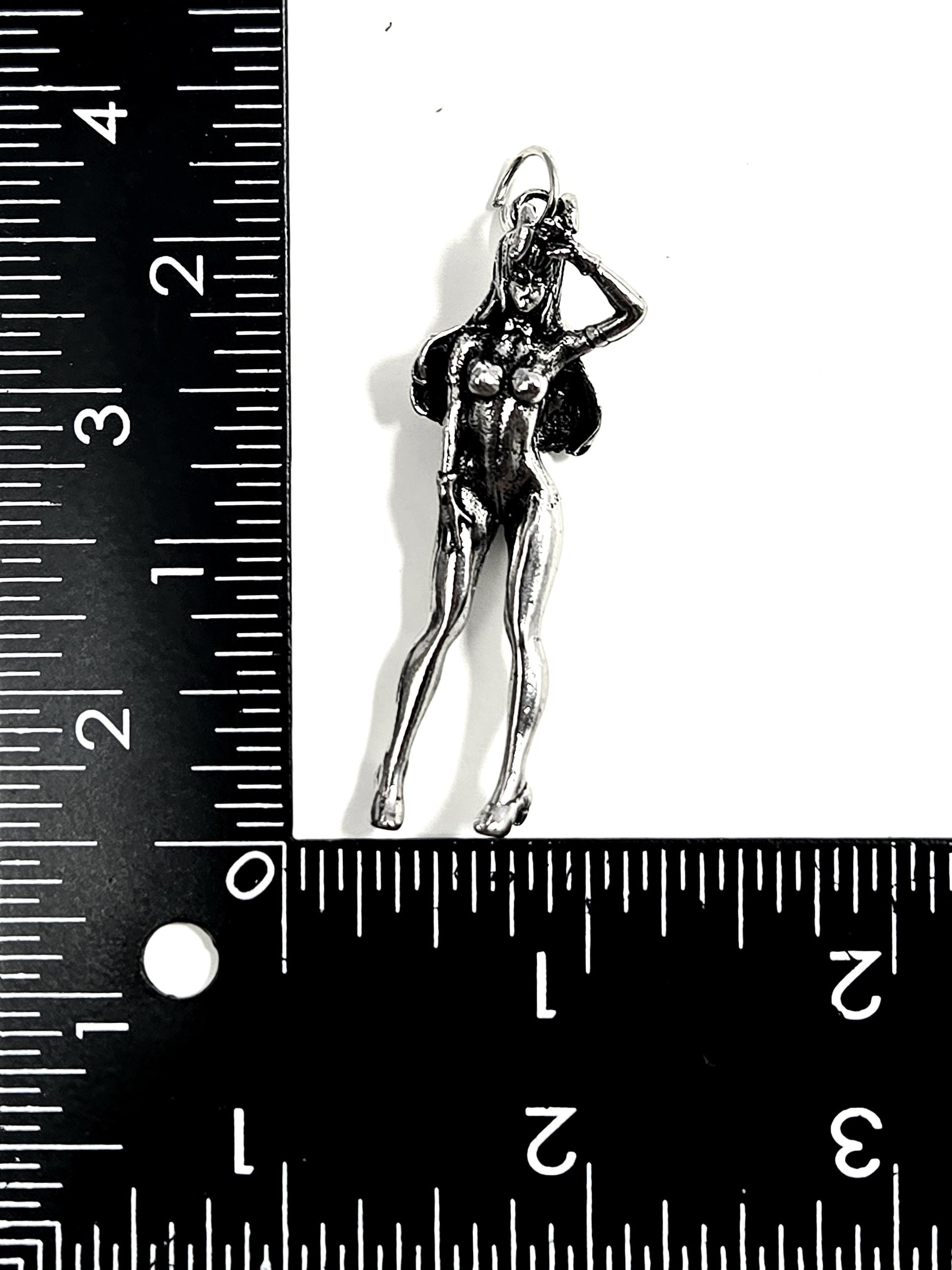 A silver-colored pendant in the shape of a female figure is placed next to a ruler for size comparison.