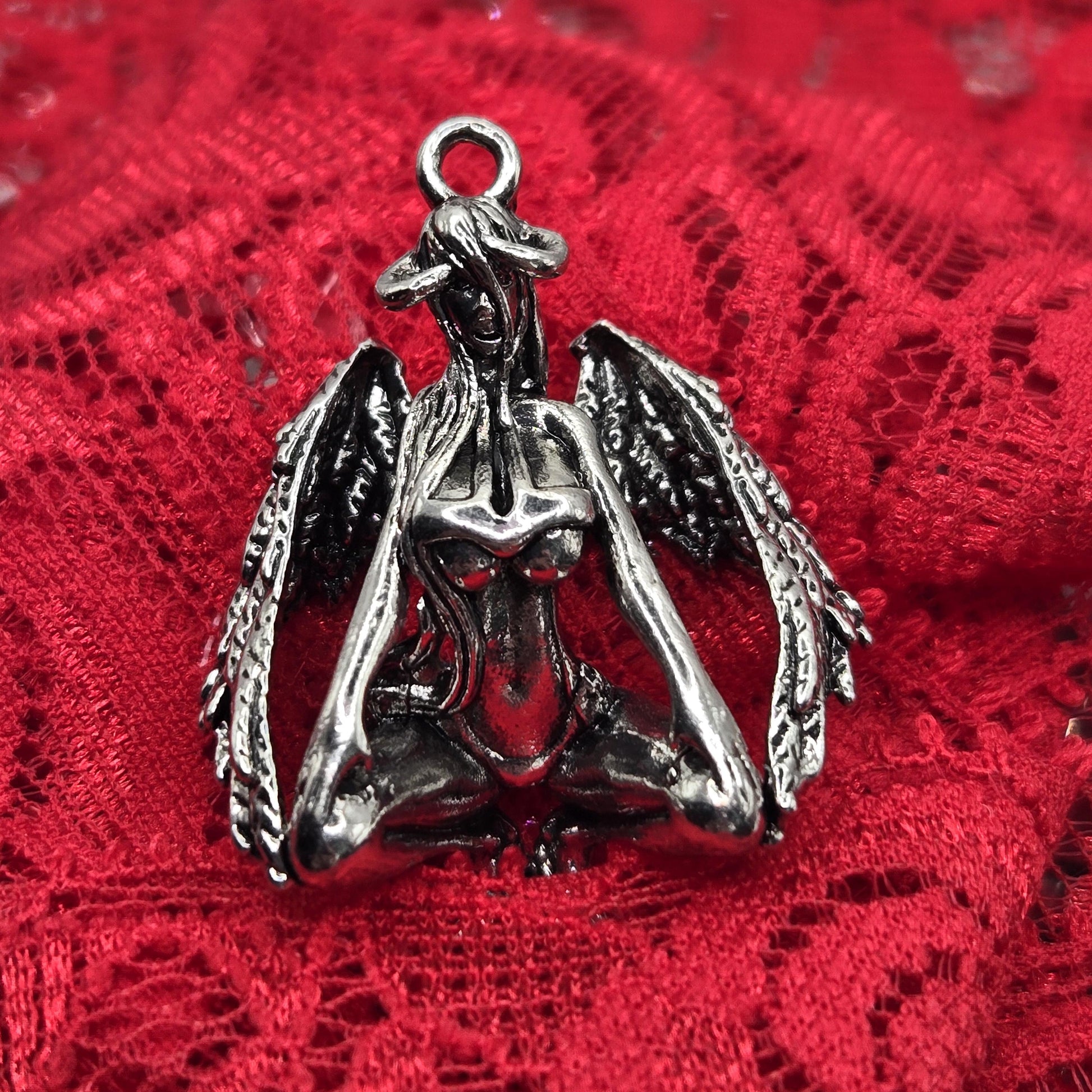 A silver metal pendant in the shape of a winged figure, resting on a red lace background.