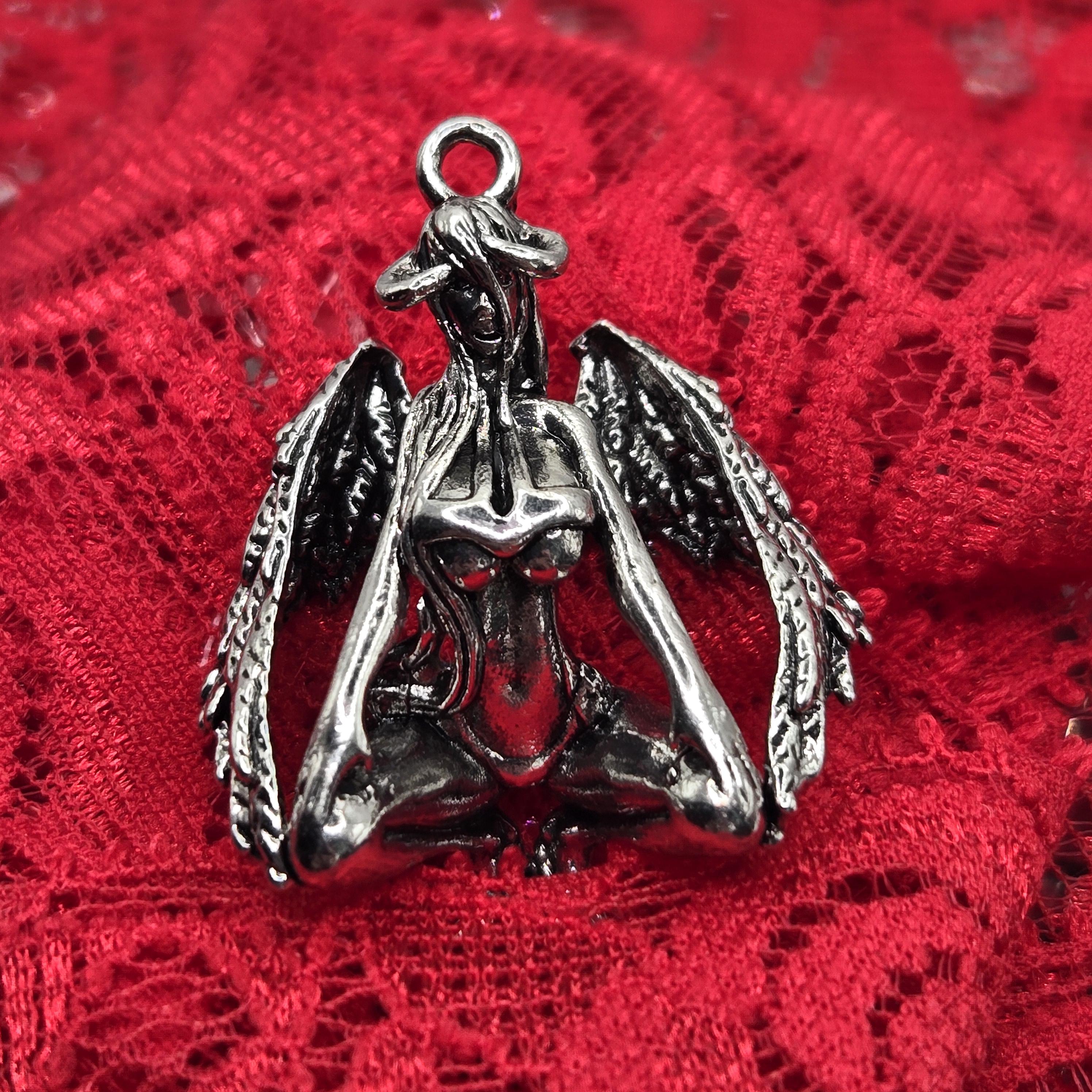 A silver metal pendant in the shape of a winged figure, resting on a red lace background.