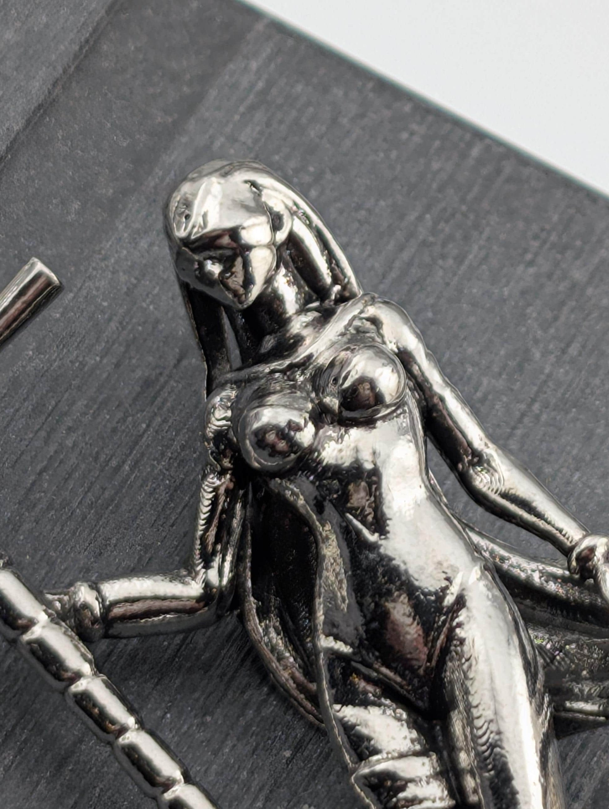 A close-up view of a shiny, metallic sculpture depicting a female figure with a flowing, draped figure.