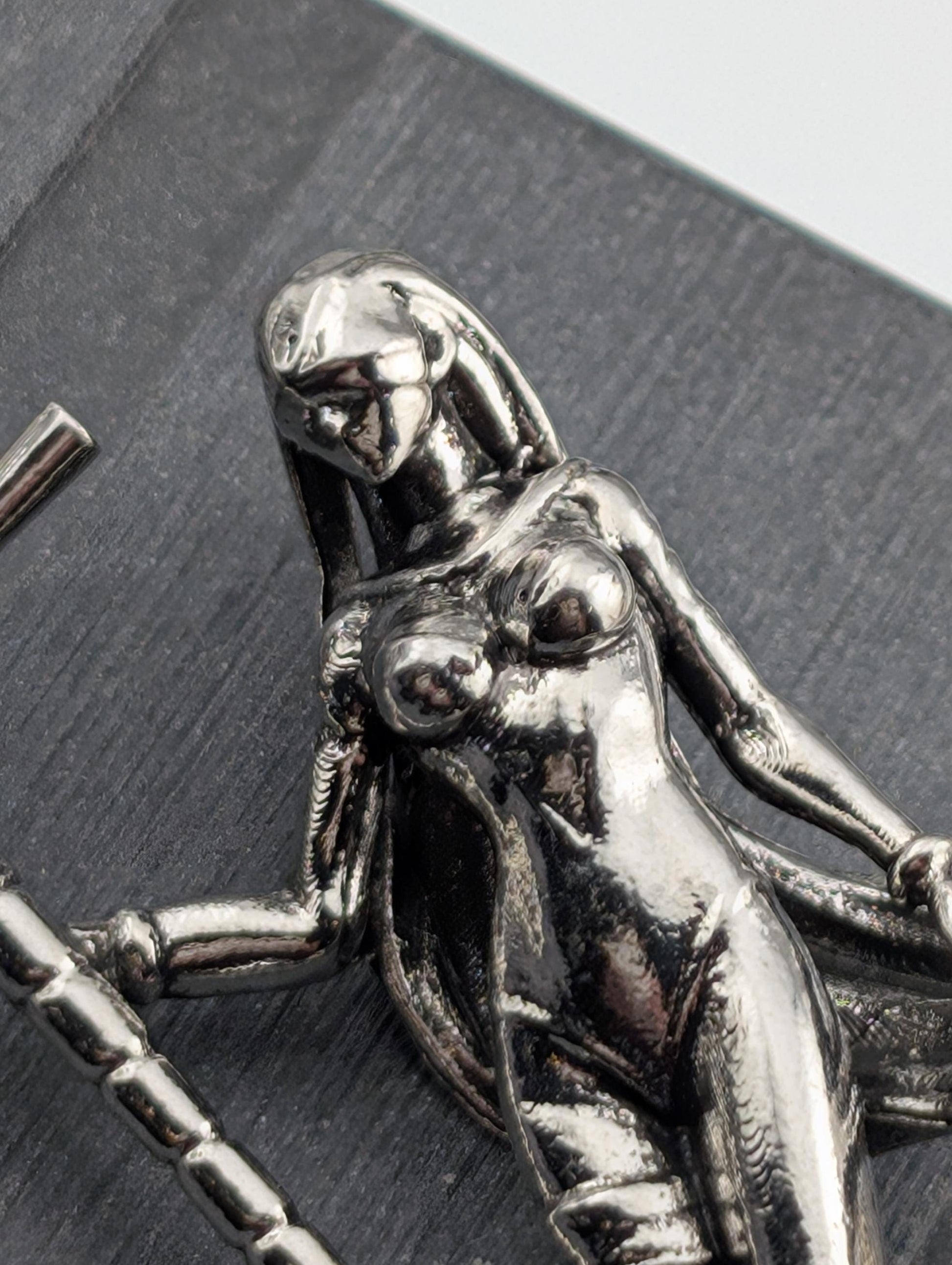 A close-up view of a shiny, metallic sculpture depicting a female figure with a flowing, draped figure.