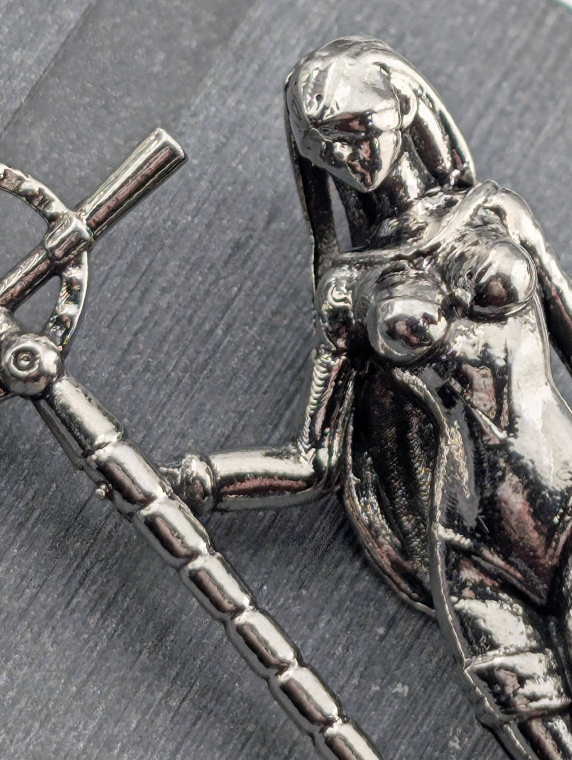A close-up view of a shiny metal sculpture depicting a female figure with a cross-like object in her hand.