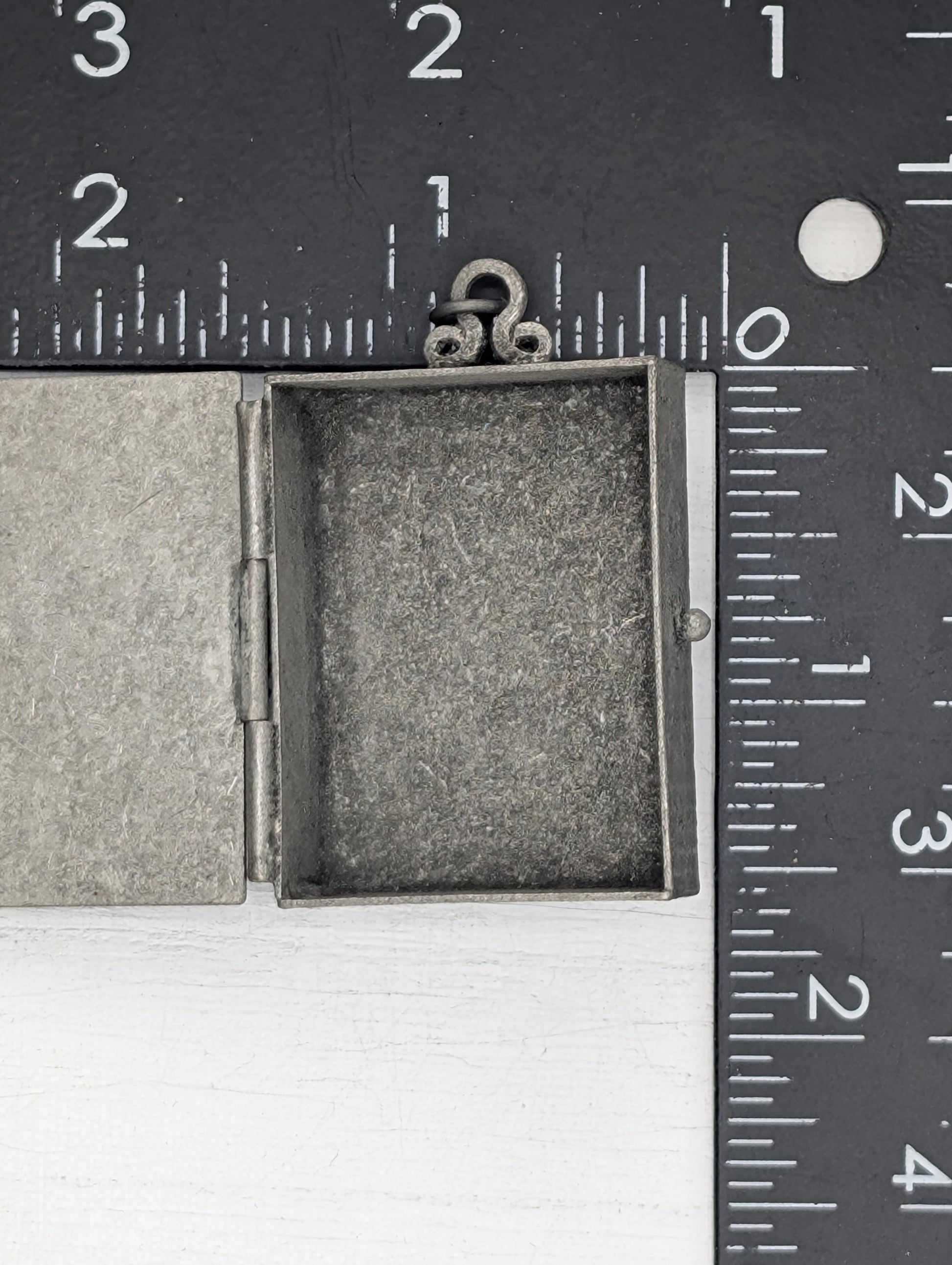 a small, open metal box with a metal clasp, placed next to a ruler for size comparison.