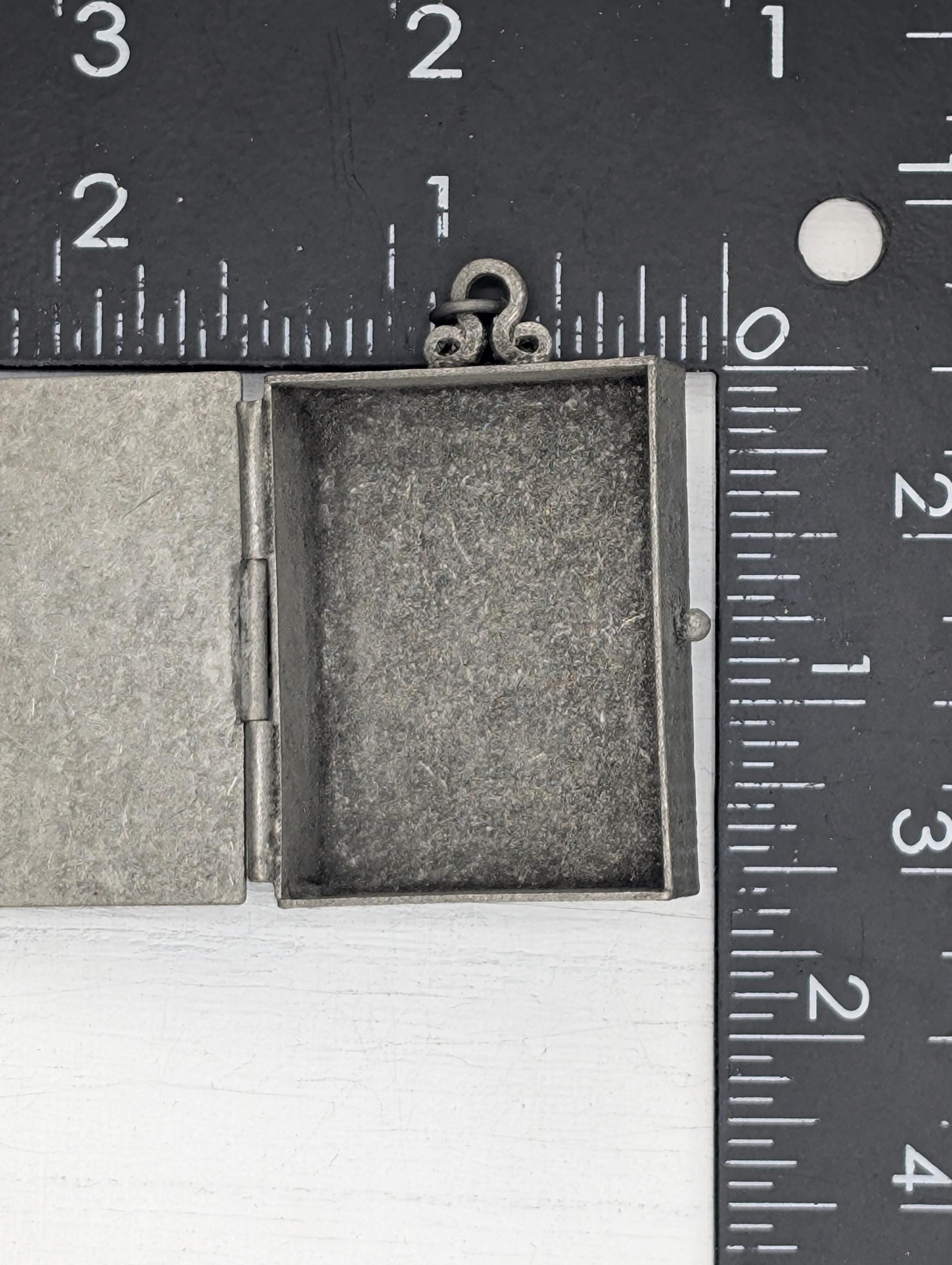 a small, open metal box with a metal clasp, placed next to a ruler for size comparison.