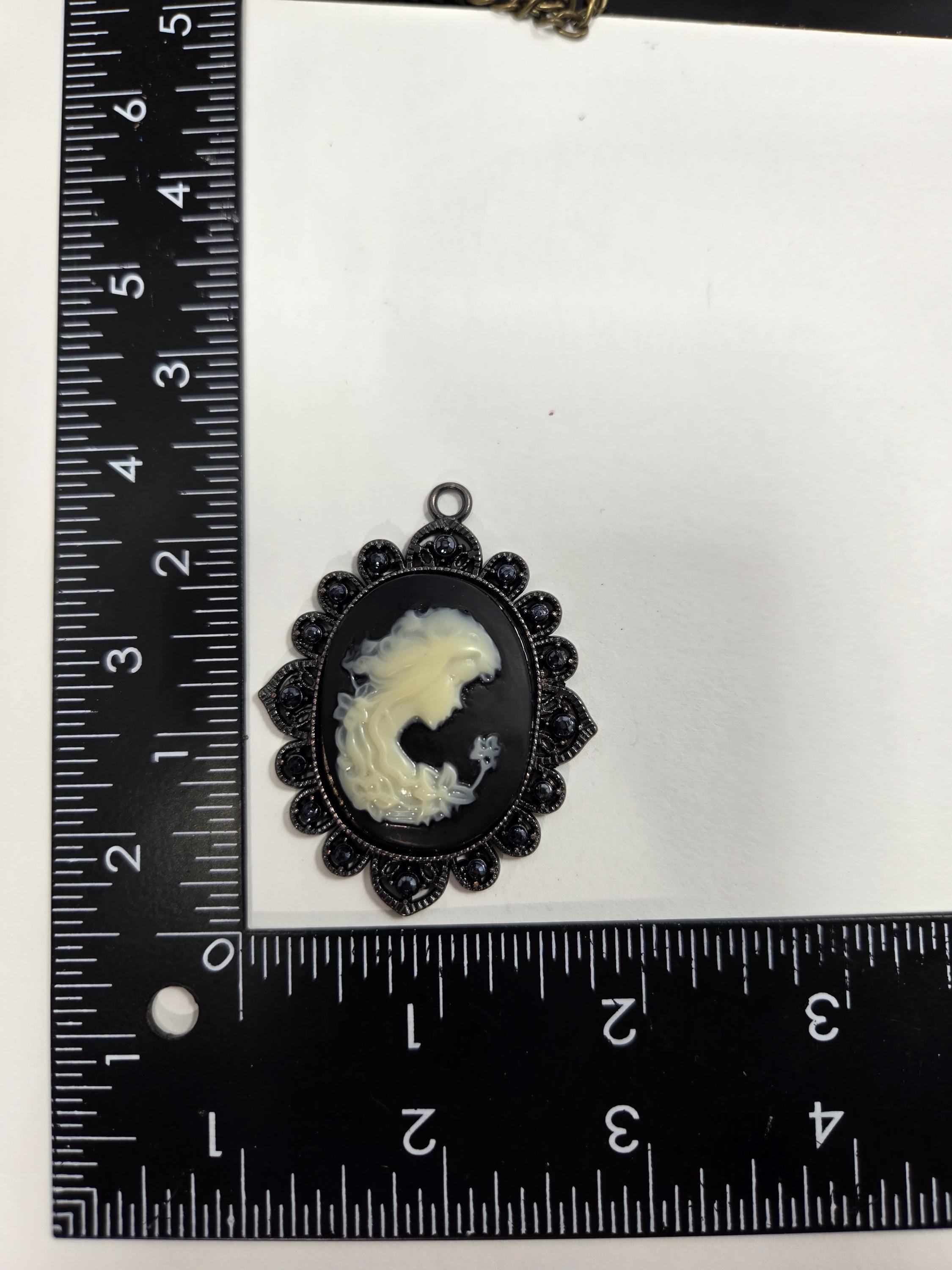 a pendant with a black oval shape and a white design, placed next to a ruler for size comparison.