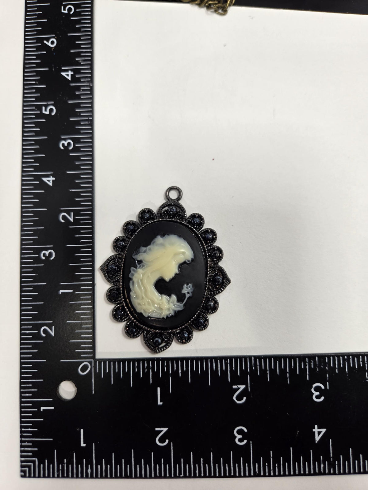 a pendant with a black oval shape and a white design, placed next to a ruler for size comparison.