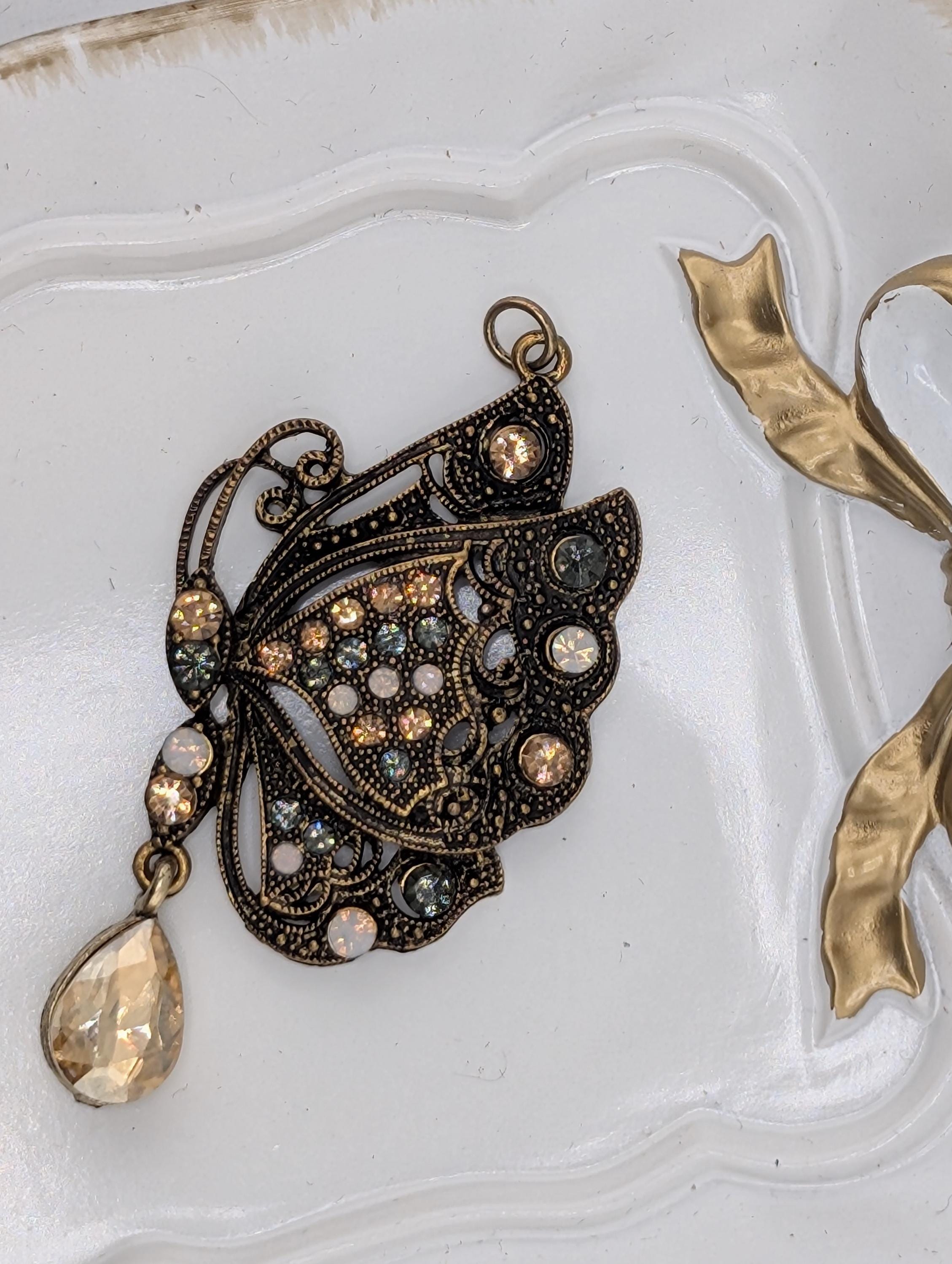a decorative butterfly pendant with a crystal or gemstone design, placed on a white surface.