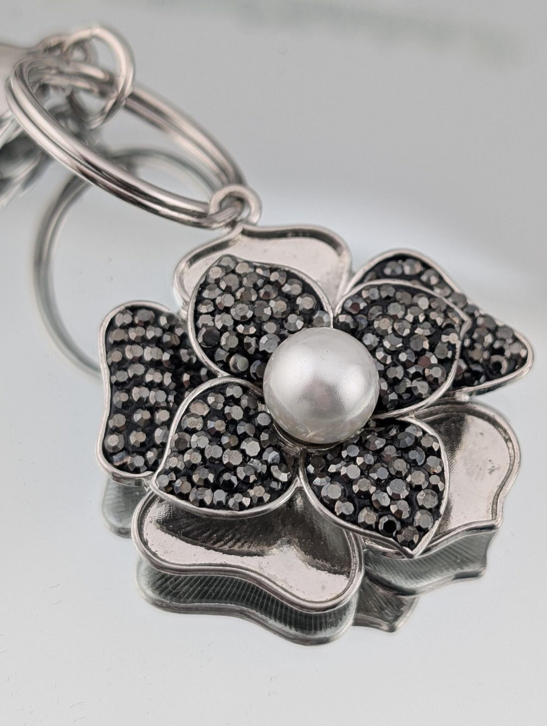 A silver-toned pendant with a large pearl at the center, surrounded by a flower-shaped design with black and white gemstones.