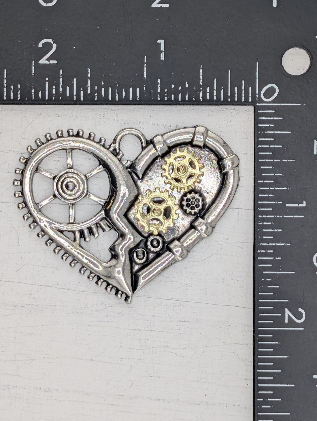 A silver heart-shaped pendant with gears and a wheel attached to it, hanging from a chain.