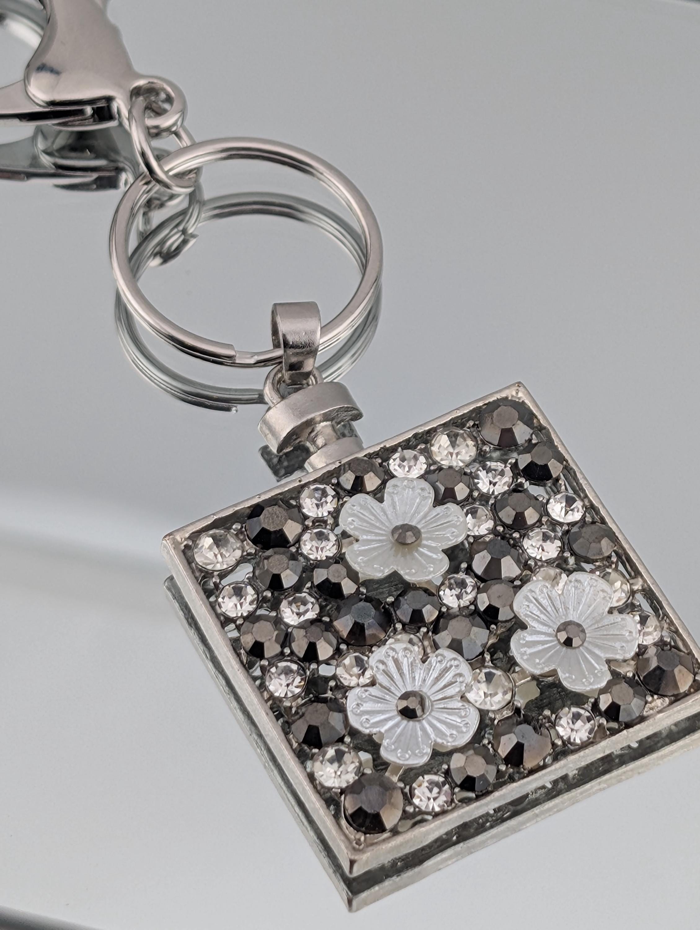 A silver keychain with a square-shaped pendant featuring a floral design and sparkling rhinestones.