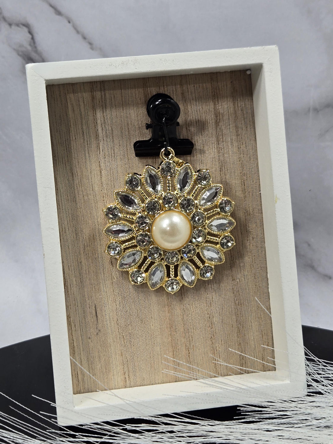 A decorative pendant with a large pearl at its center, surrounded by numerous sparkling gemstones in a gold and white design.