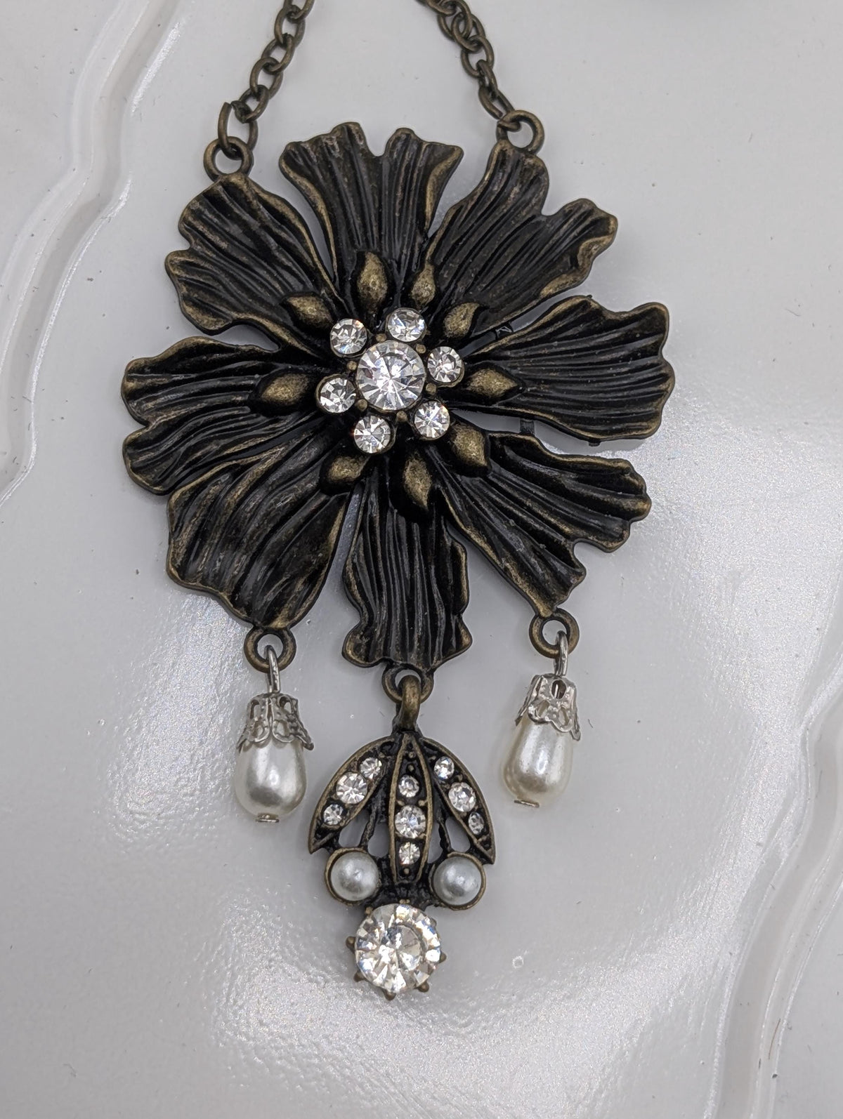 A decorative pendant featuring a large black flower-shaped design with a central crystal surrounded by smaller pearls and diamonds.