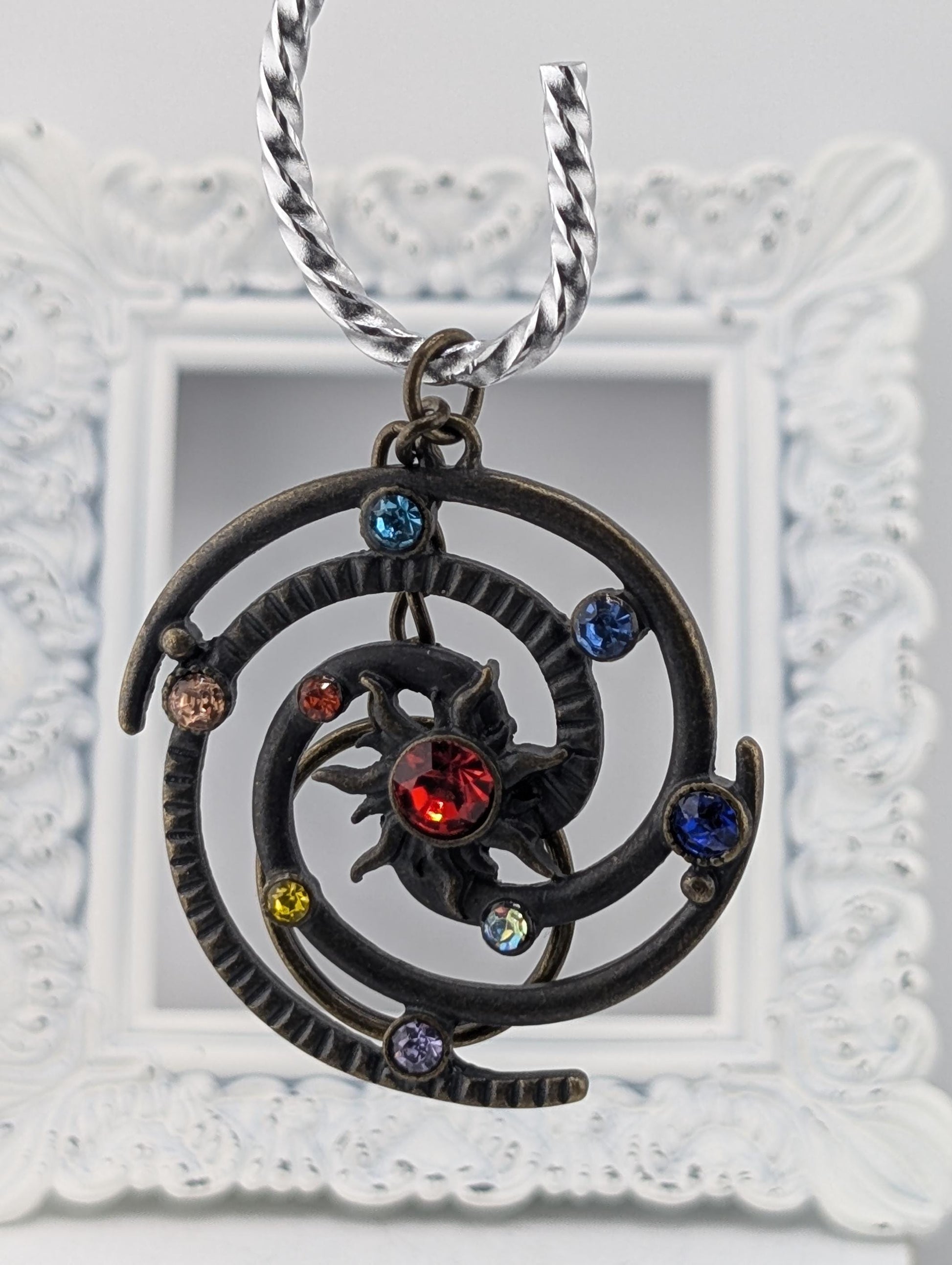A decorative pendant with a spiral design and colorful gemstones, suspended from a chain.