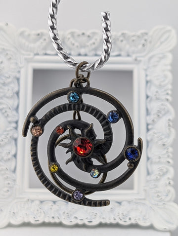 A decorative pendant with a spiral design and colorful gemstones, suspended from a chain.