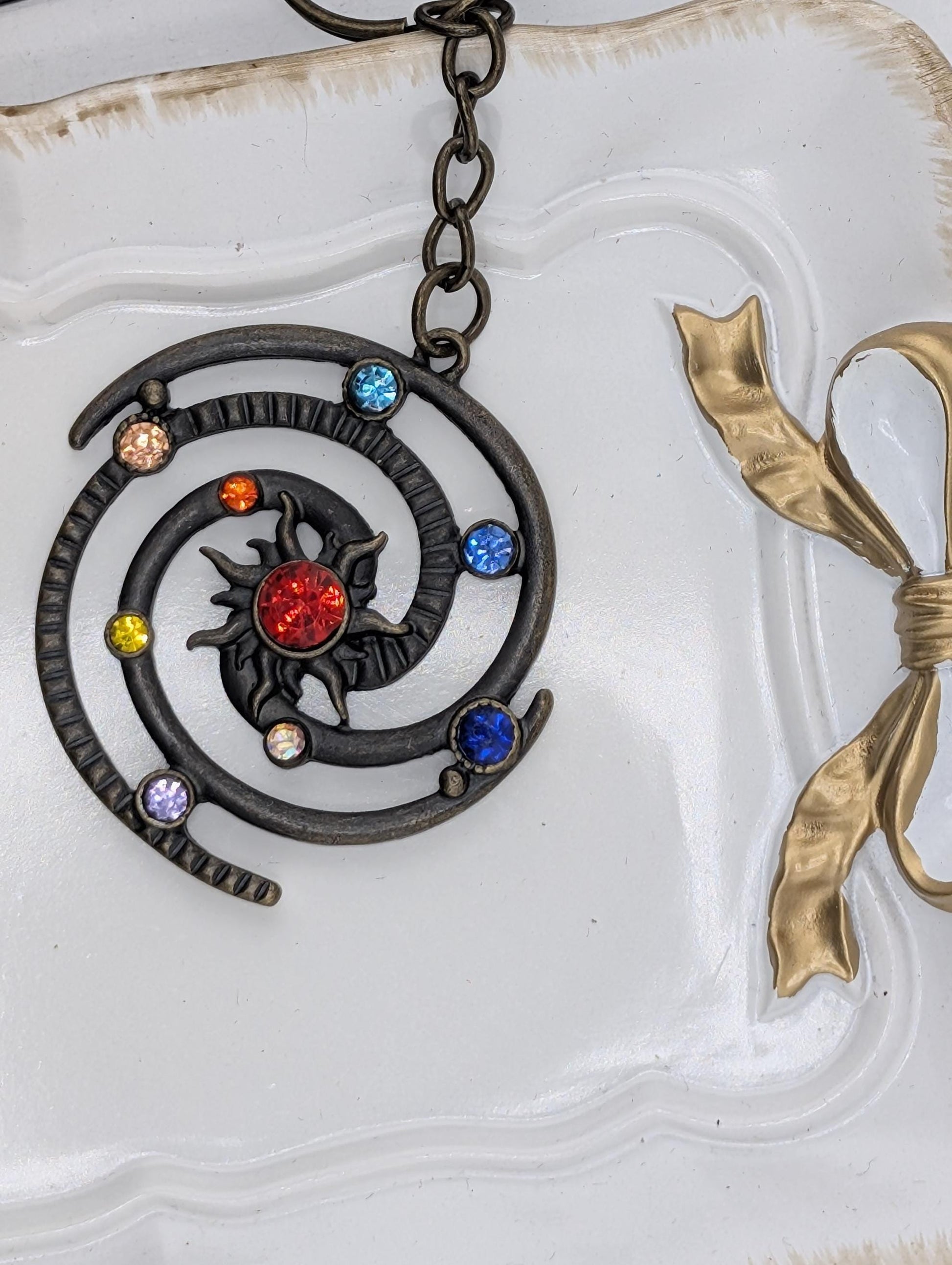 A decorative pendant with a spiral design and colorful gemstones, hanging from a chain.