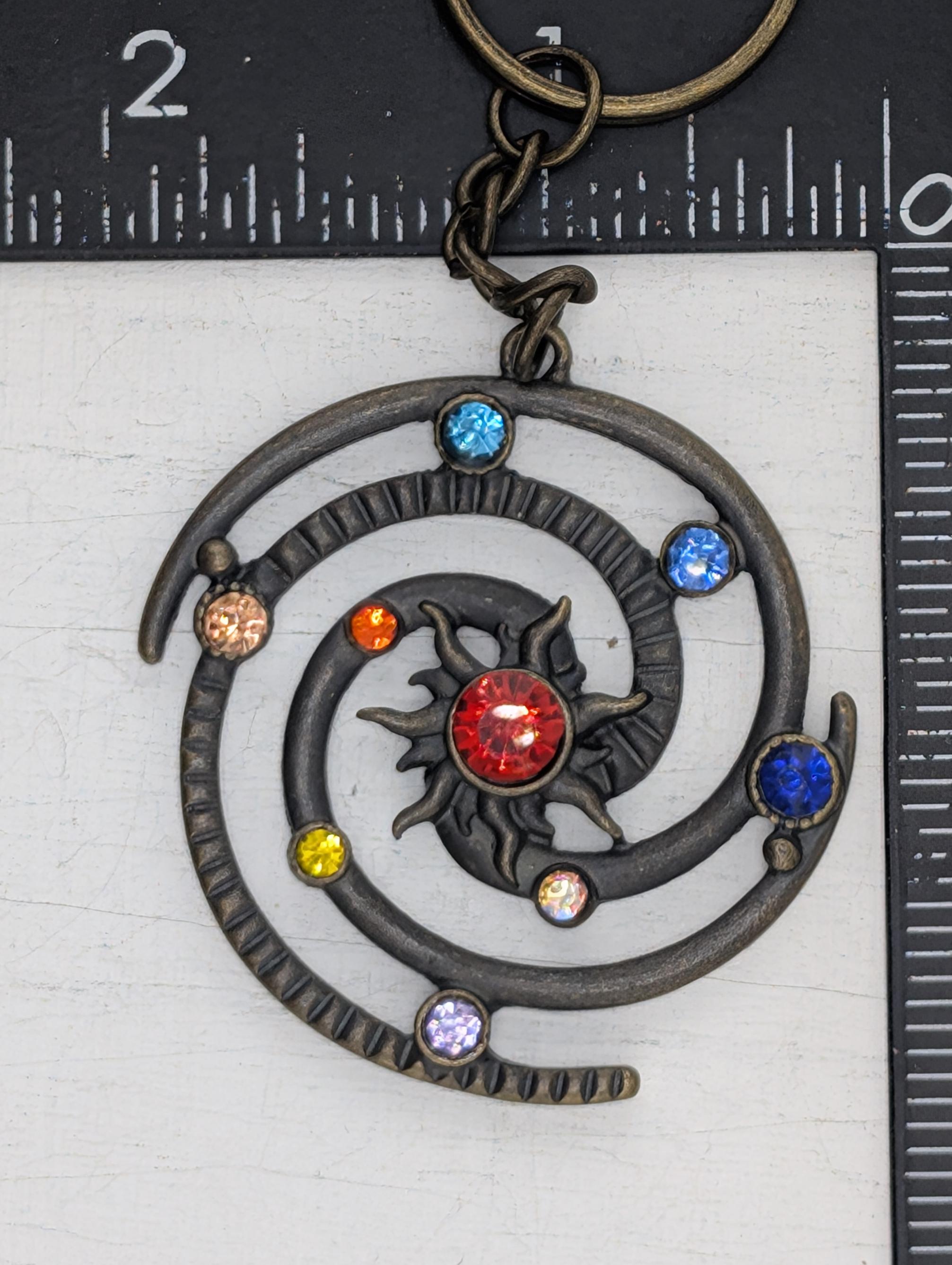 A decorative metal pendant with a spiral design and colorful gemstones, including a red gemstone at the center.