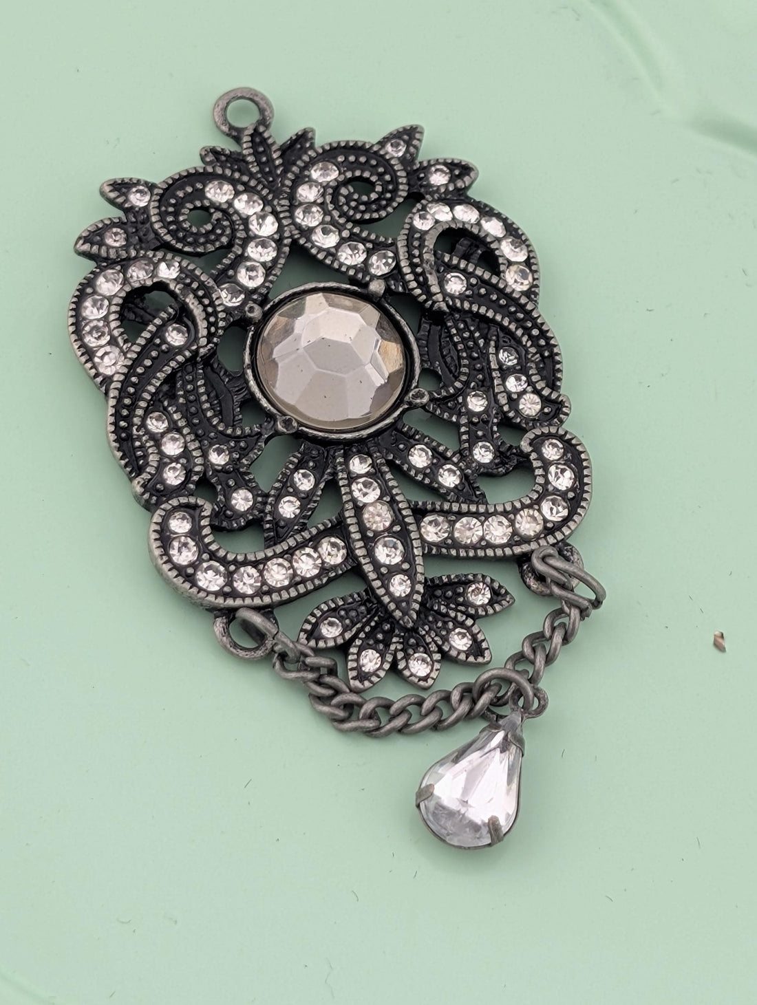 A decorative pendant with a large crystal at the center, surrounded by intricate metalwork and a dangling crystal element.