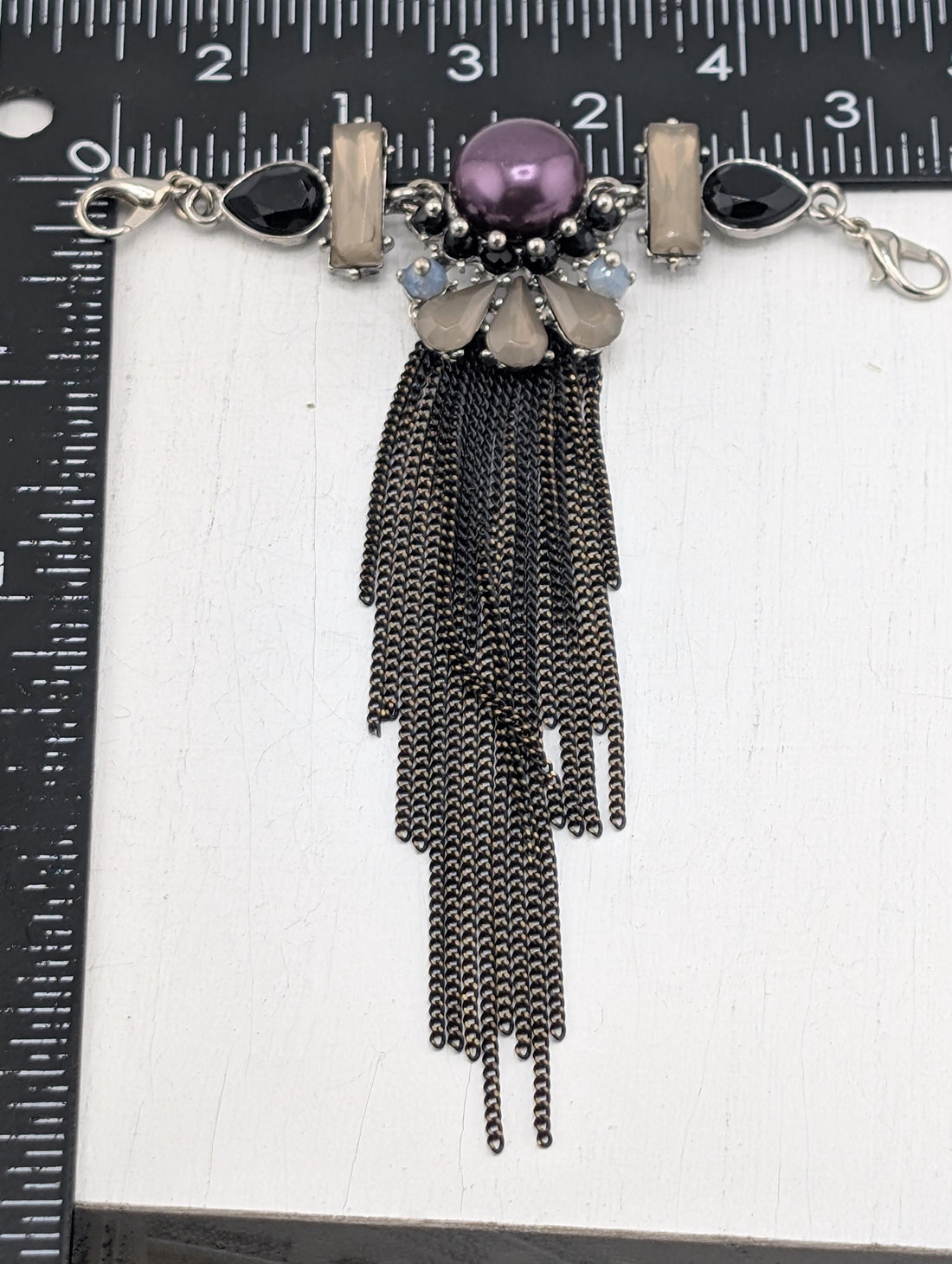 A close-up view of a decorative necklace with various beads, charms, and a large purple gemstone.