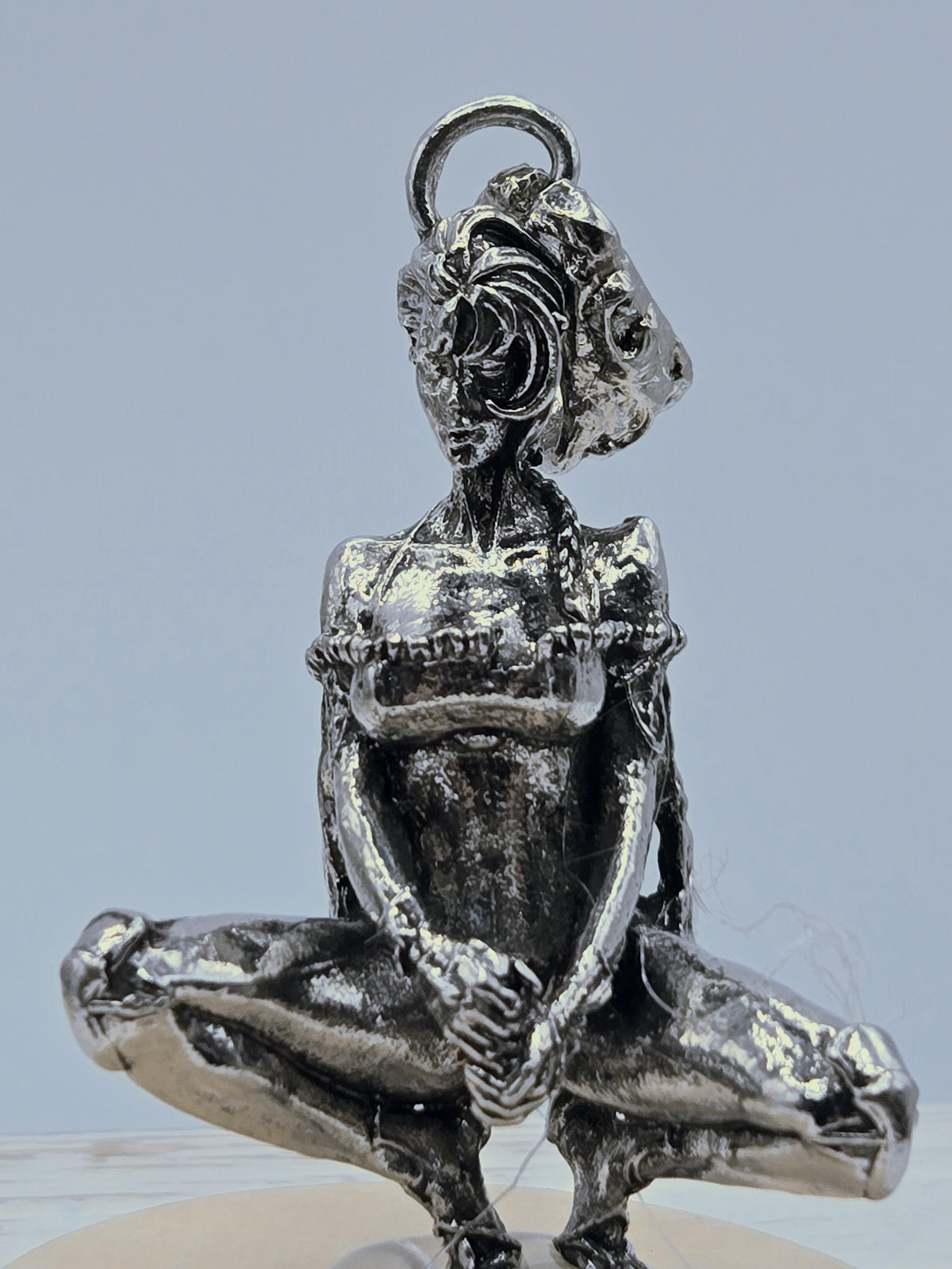 A close-up view of a shiny, metallic object resembling a pendant or charm, with intricate details and a textured surface.