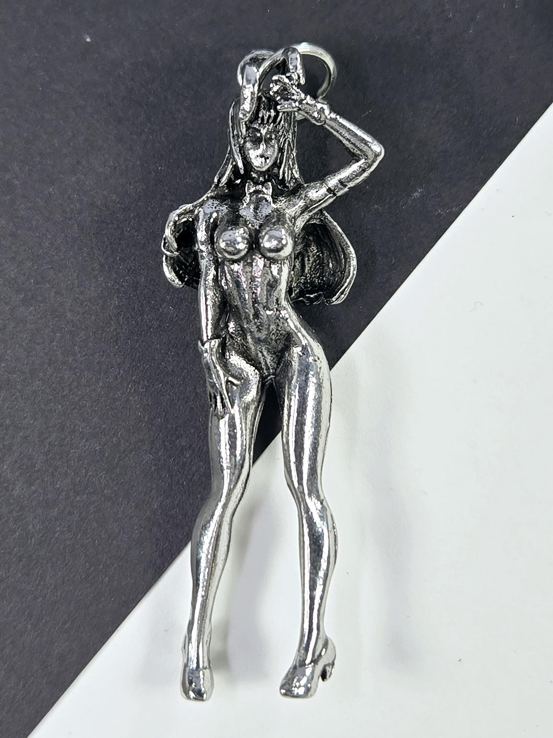 A silver-colored metal pendant in the shape of a female figure, with a wing-like design on her back and a detailed, sculpted appearance.