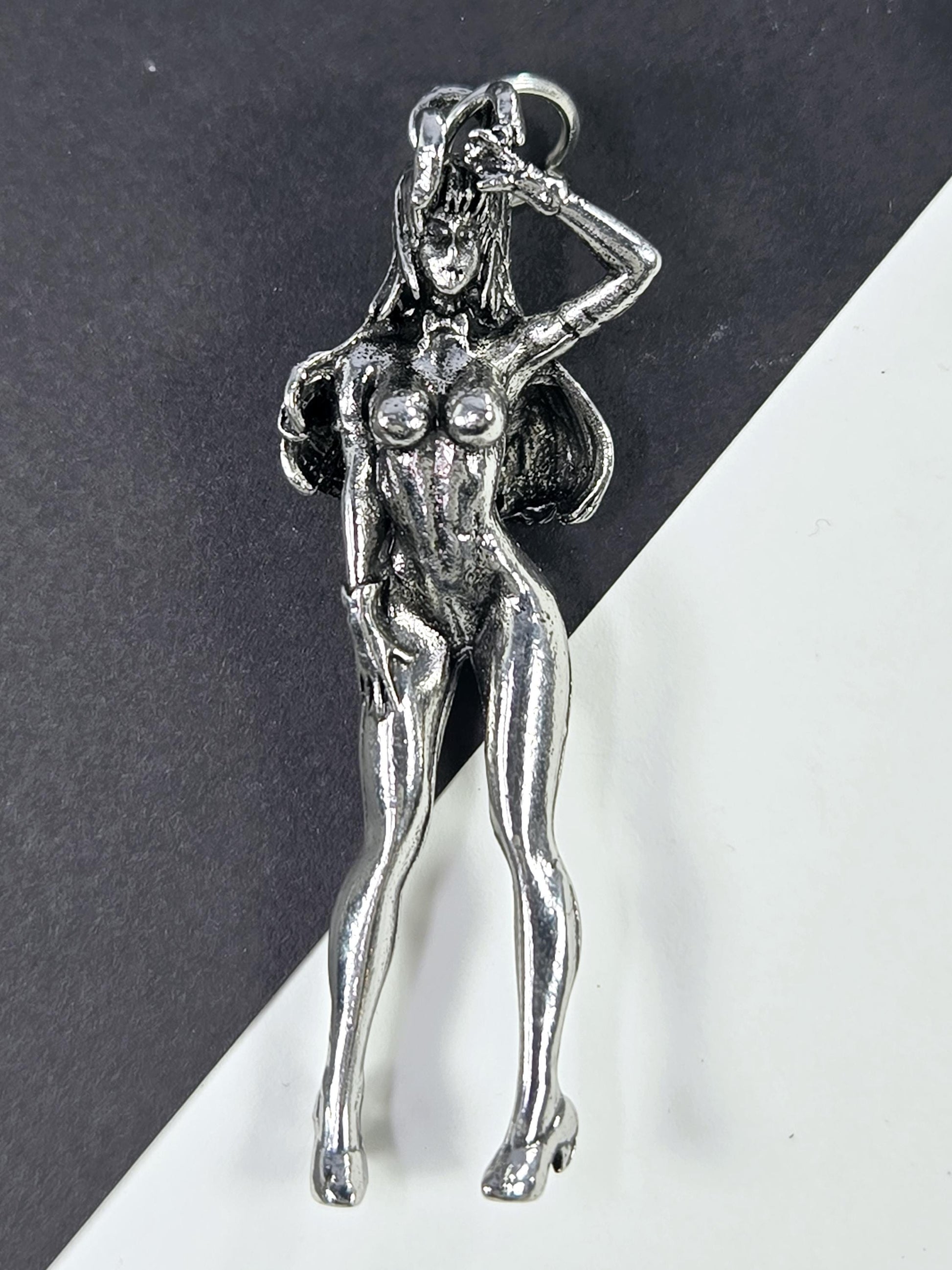 A silver-colored metal pendant in the shape of a female figure, with a wing-like design on her back and a detailed, sculpted appearance.