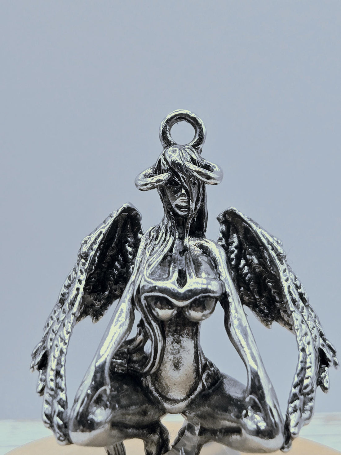 A silver-colored metal charm in the shape of a bird, with intricate details and a textured appearance.