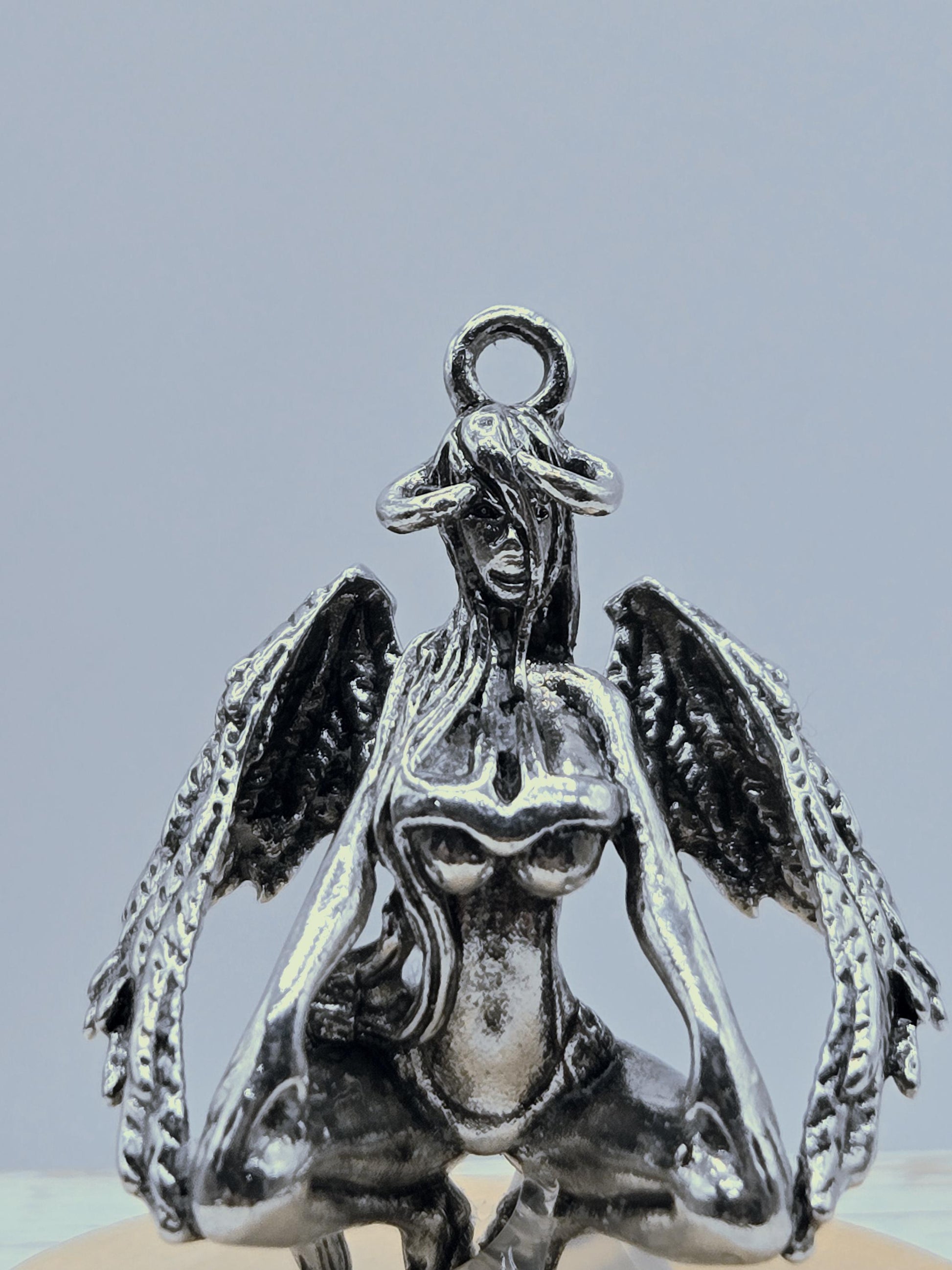 A silver metal sculpture of a winged creature with intricate details and a metallic sheen.