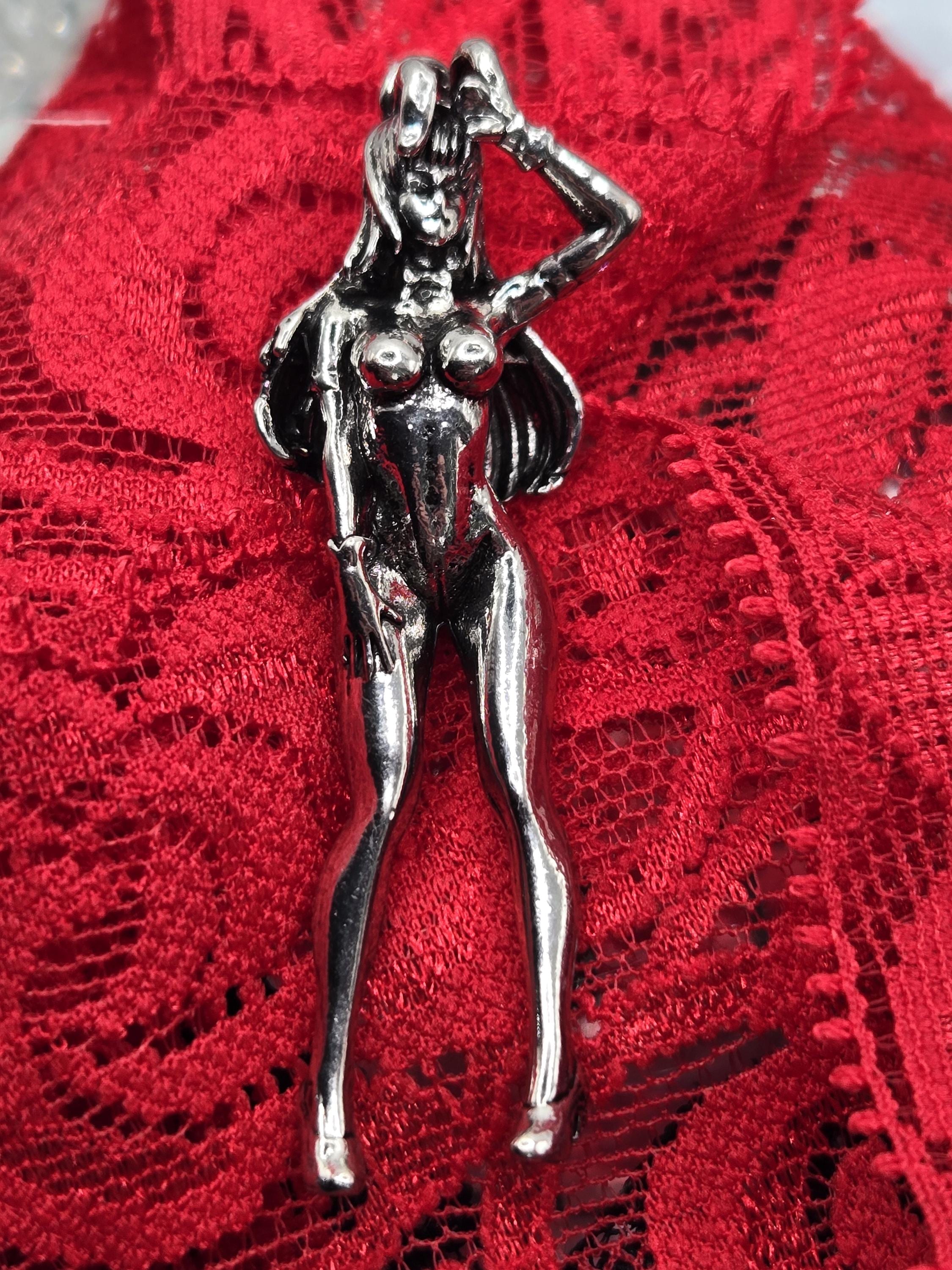A shiny metal figurine of a woman is displayed on a red lace background.