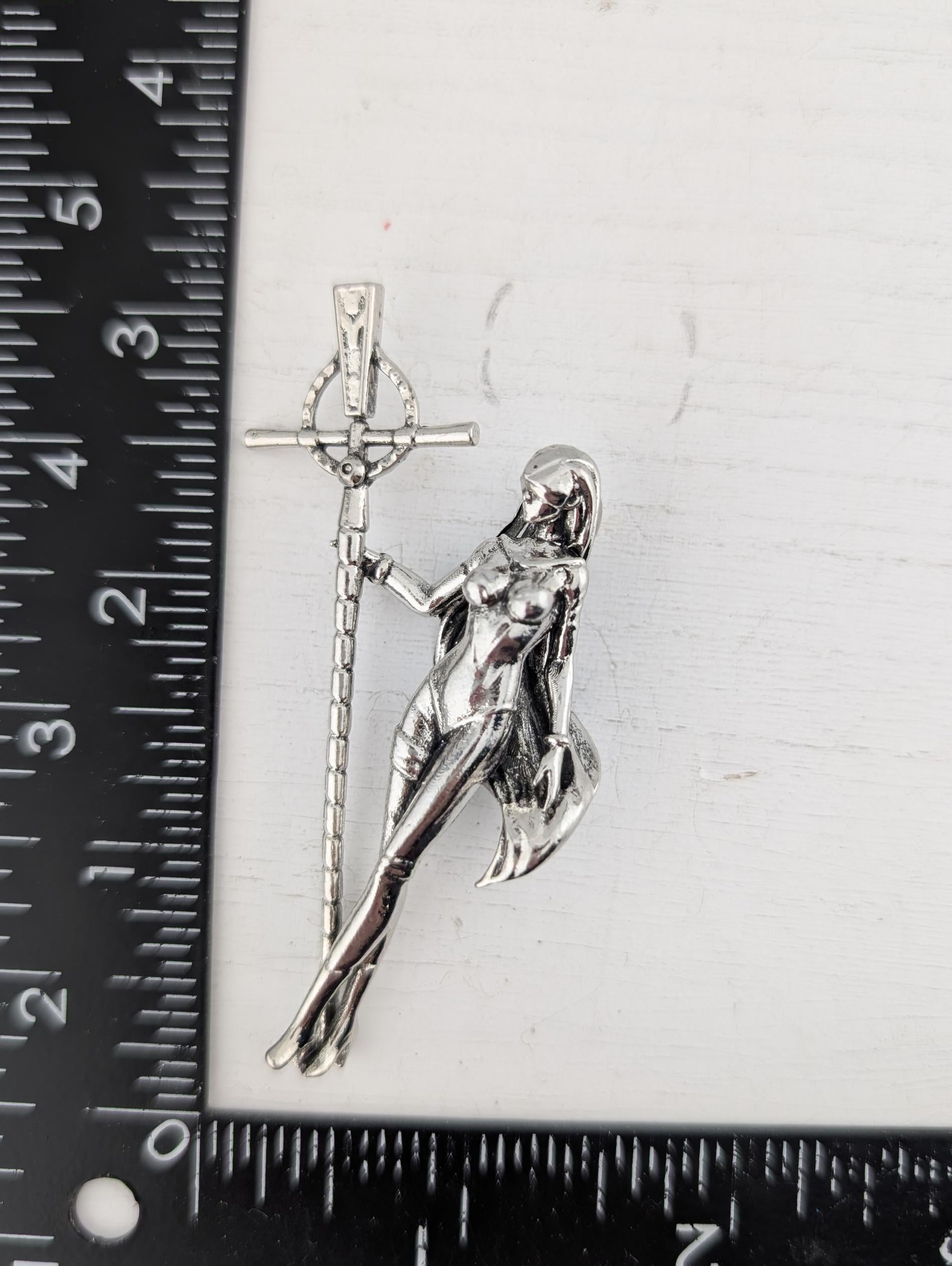 A silver-colored metal brooch or pendant in the shape of a female figure holding a cross.
