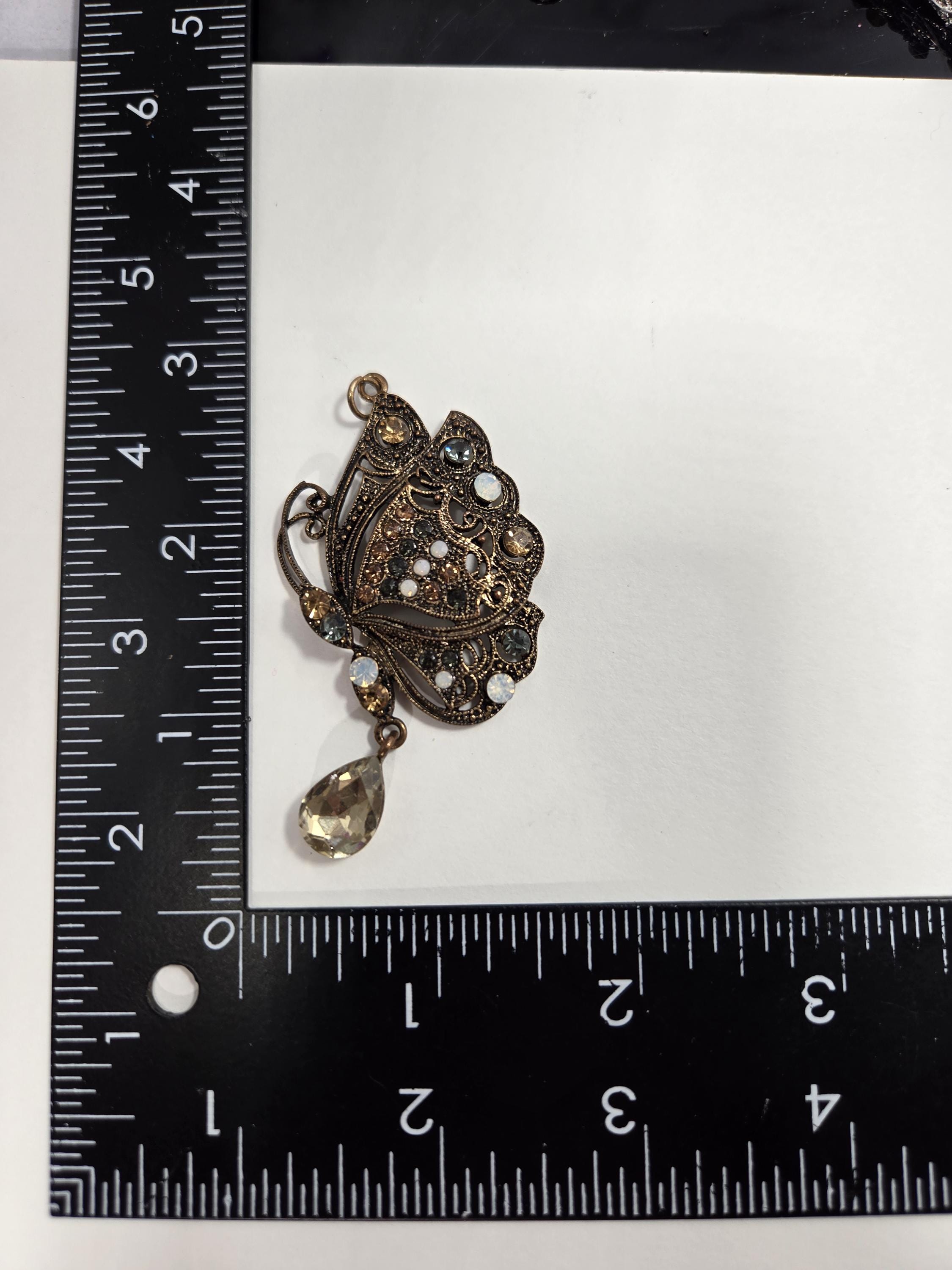 a small, ornate piece of jewelry, possibly a brooch or pendant, placed next to a ruler for size comparison.