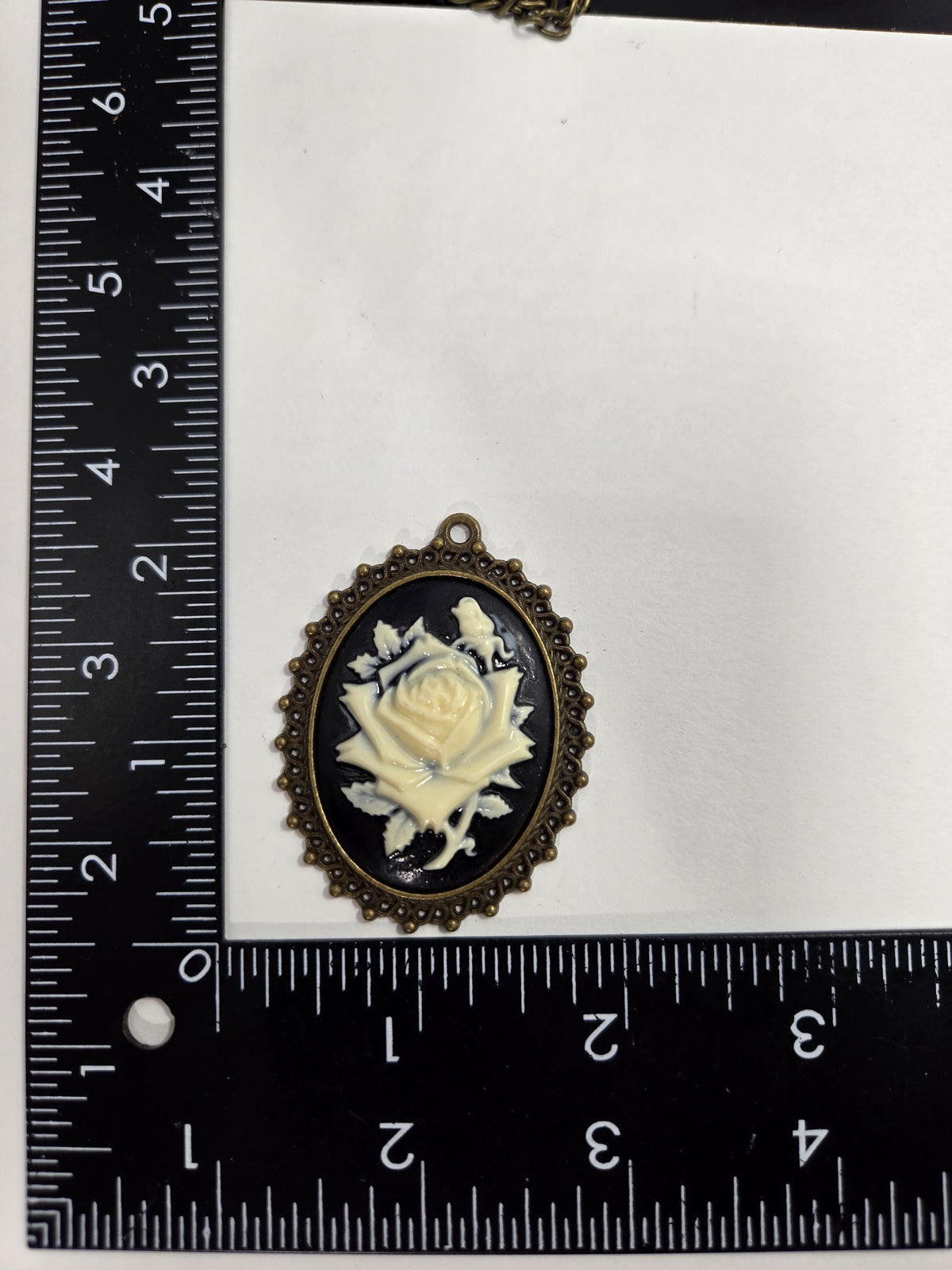 a close-up view of a pendant with a rose design, placed next to a ruler for size comparison.