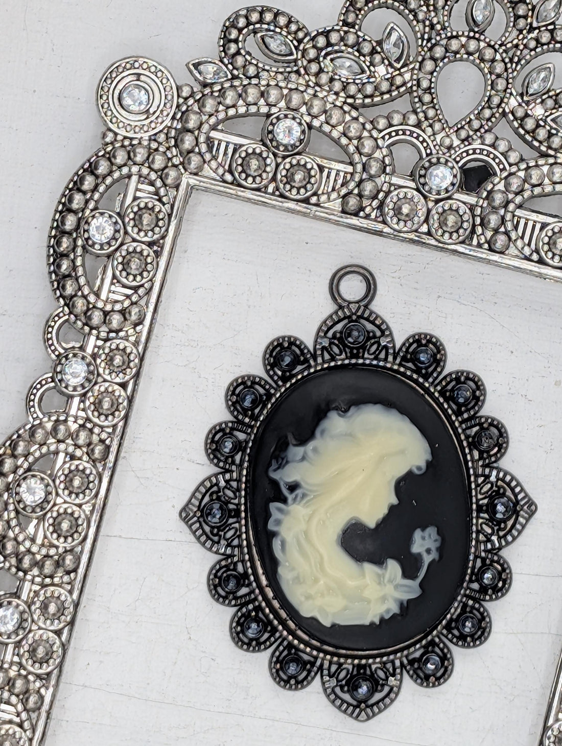 a black oval pendant with a white design, placed within an ornate silver frame.