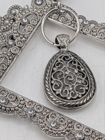A close-up image of a decorative metal pendant with intricate designs and sparkling crystals.