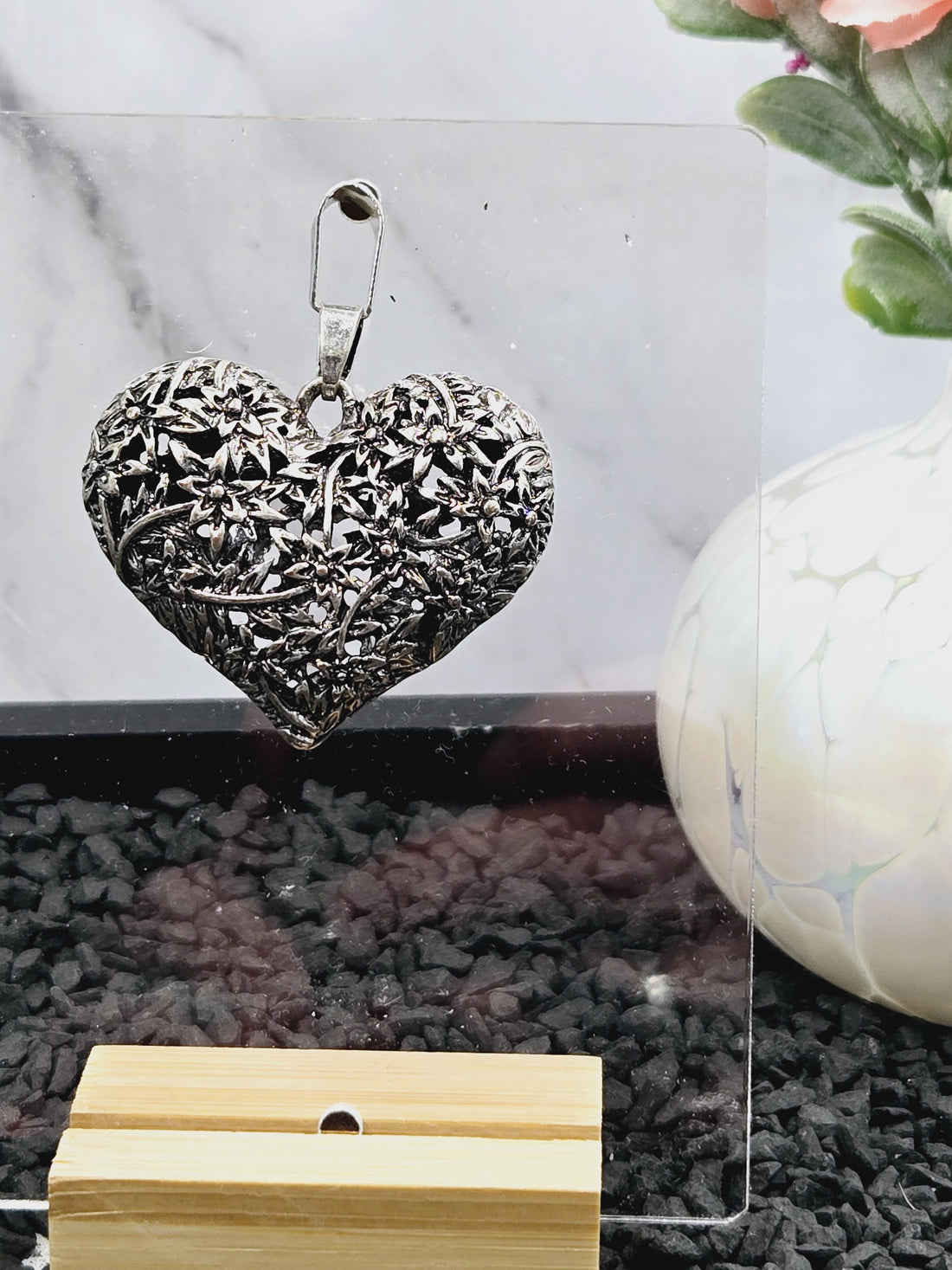 A silver heart-shaped pendant with intricate floral designs.