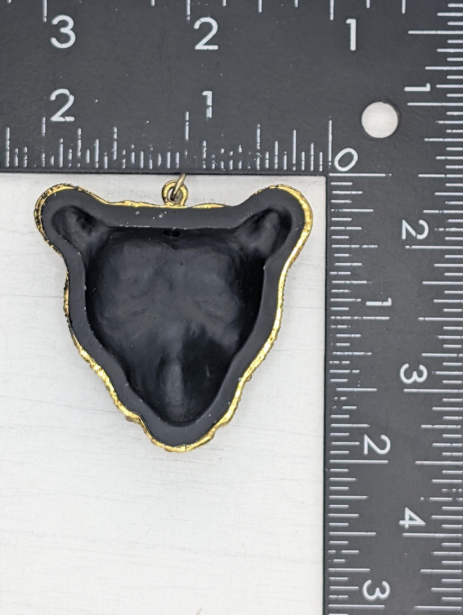 a black bear pendant with a gold-colored frame, placed next to a ruler for size comparison.