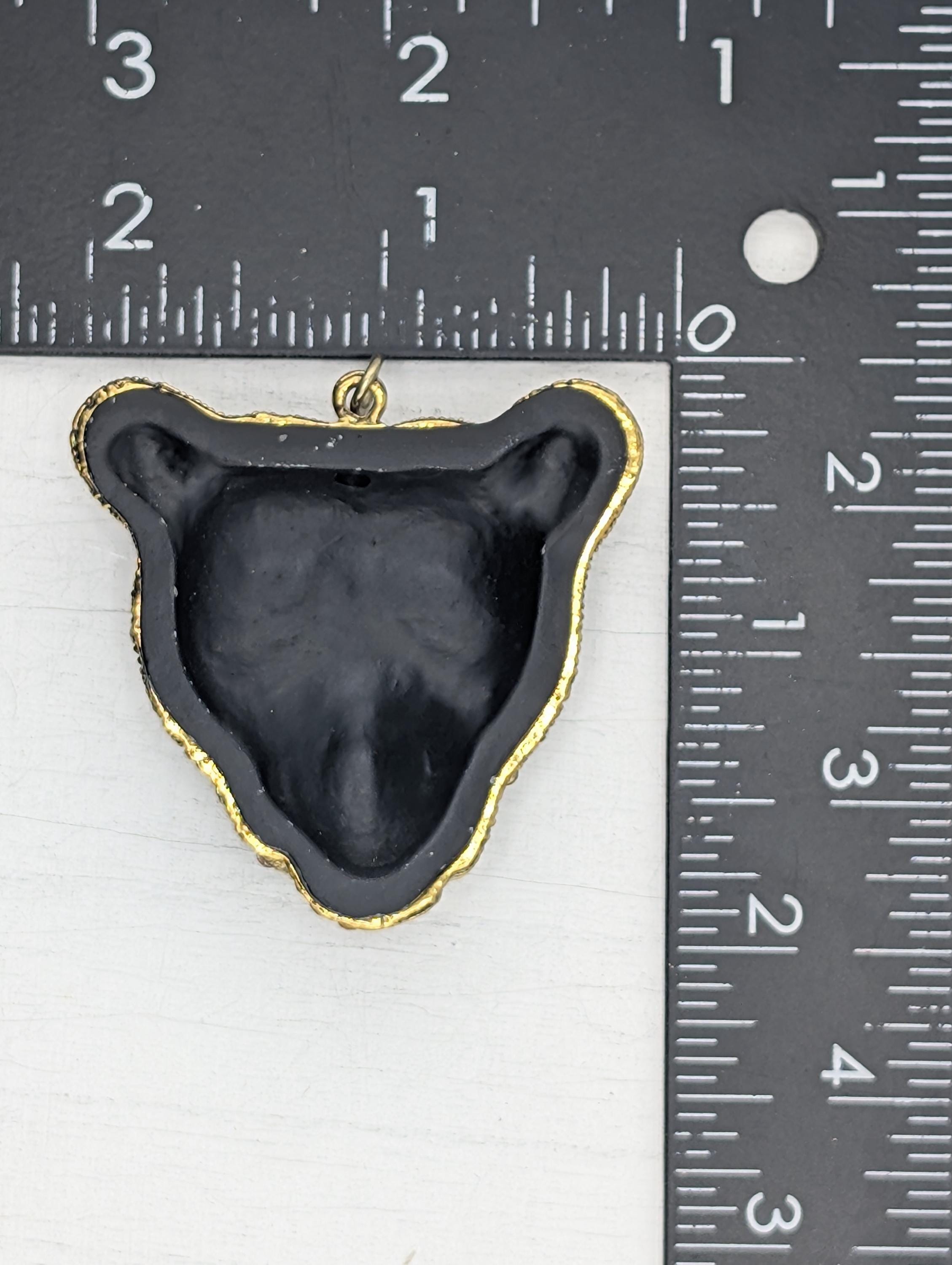 a black bear pendant with a gold-colored frame, placed next to a ruler for size comparison.