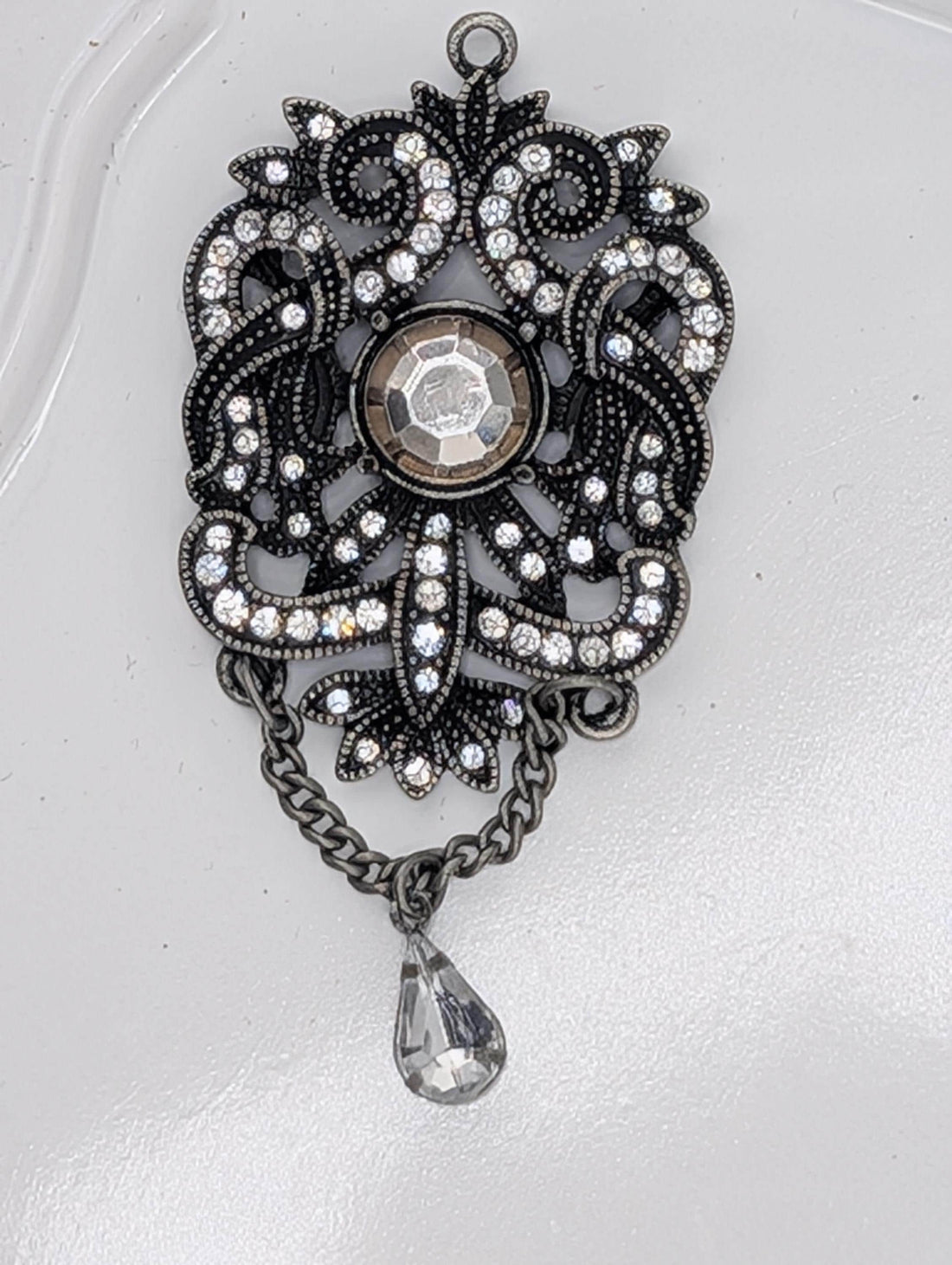 A decorative pendant with a large crystal at the center, surrounded by intricate metalwork and a dangling crystal element.