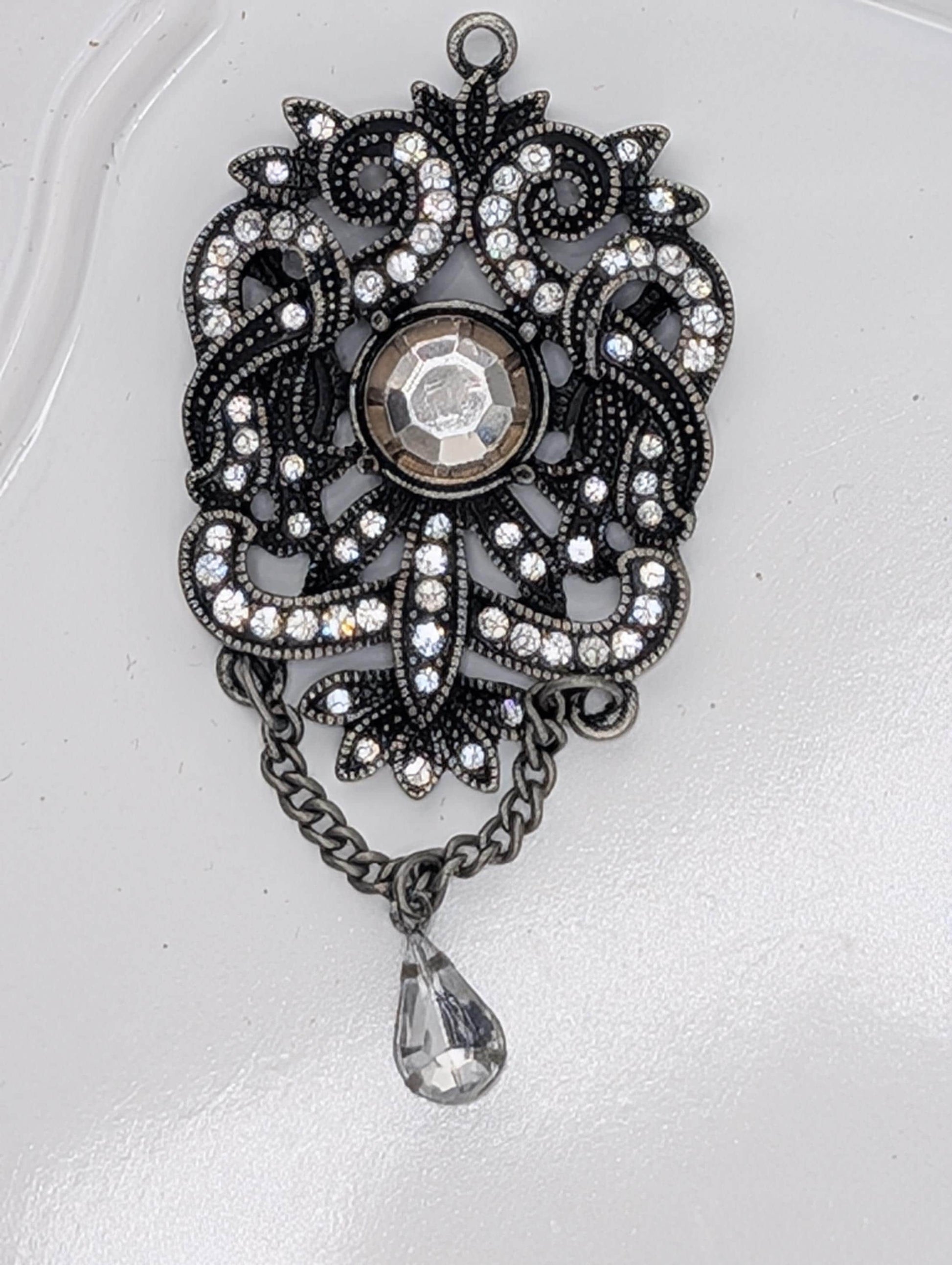 A decorative pendant with a large crystal at the center, surrounded by intricate metalwork and a dangling crystal element.