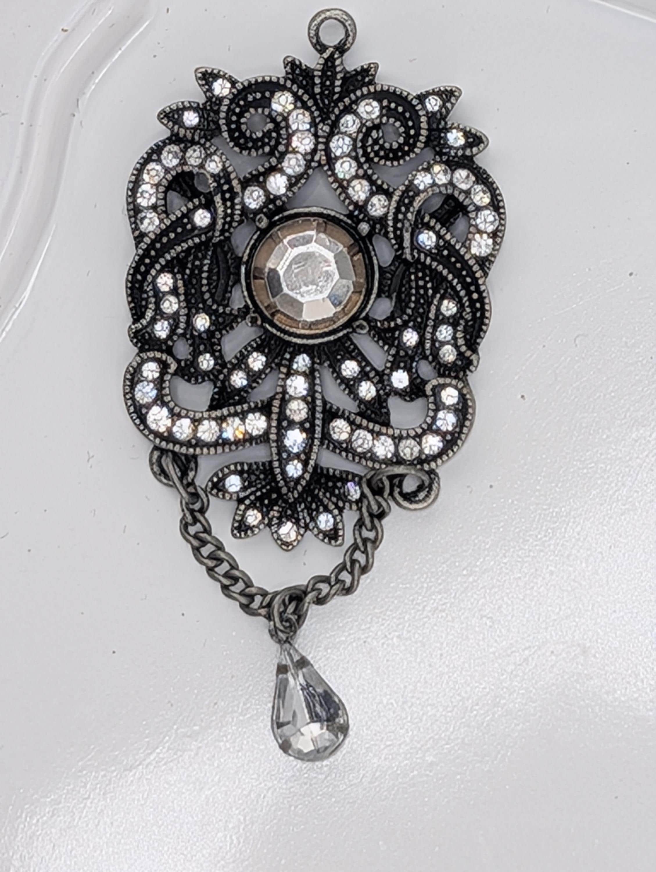 A decorative pendant with a large crystal at the center, surrounded by intricate metalwork and a dangling crystal element.