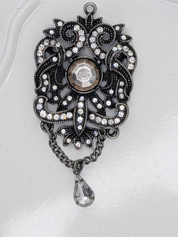 A decorative pendant with a large crystal at the center, surrounded by intricate metalwork and a dangling crystal element.