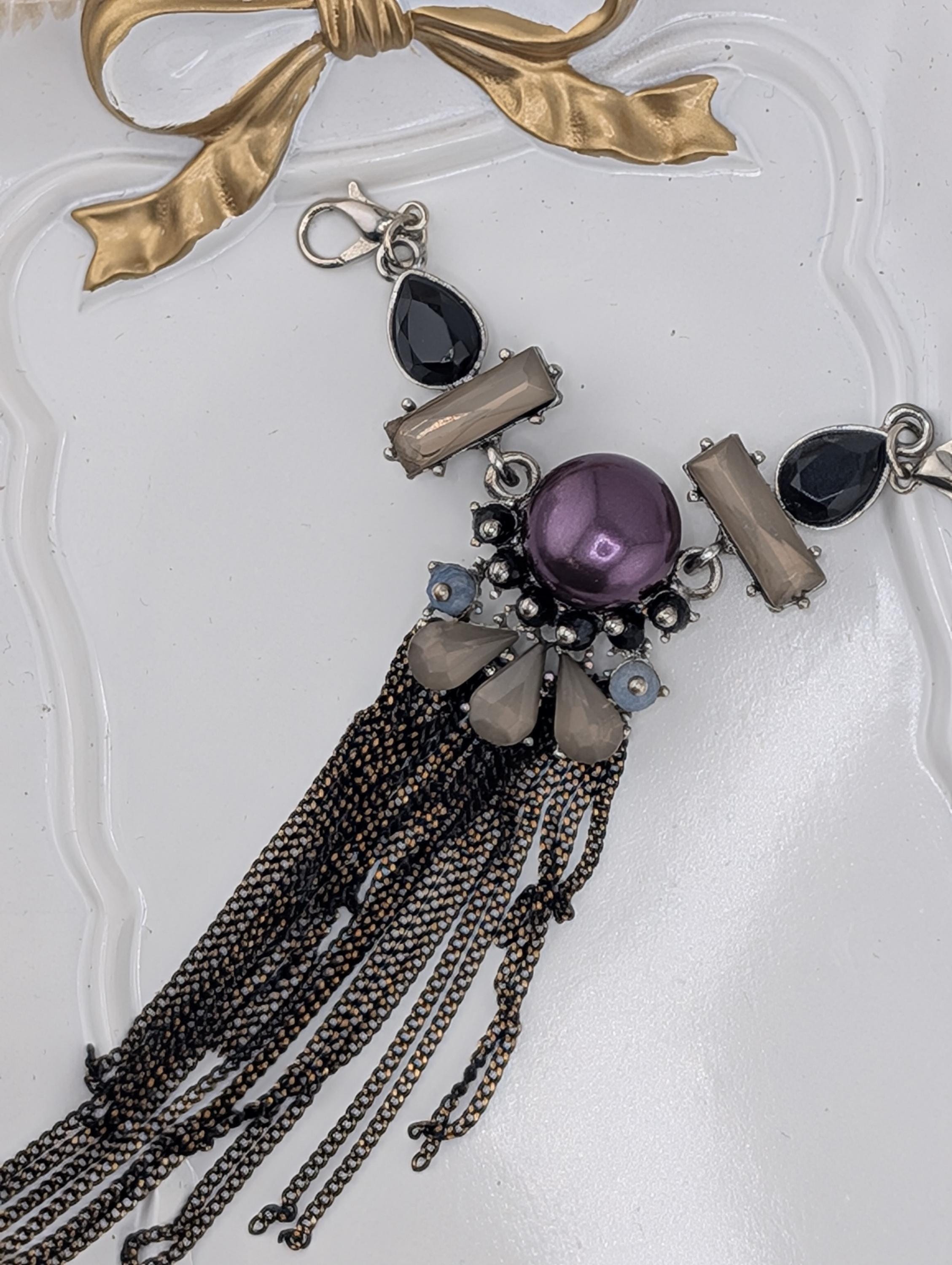 A close-up view of a decorative necklace with various beads, charms, and a large purple gemstone.