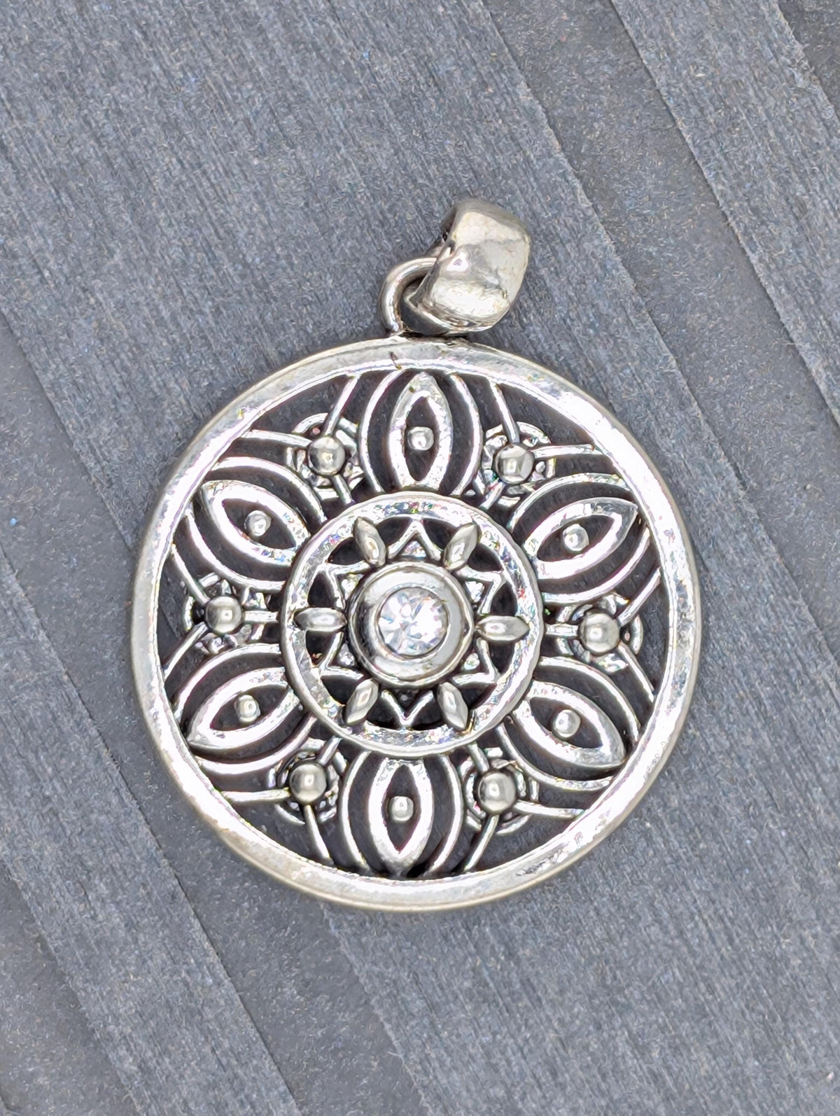 A silver pendant with an intricate design, featuring a central motif surrounded by smaller, symmetrical patterns.