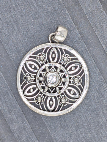 A silver pendant with an intricate design, featuring a central motif surrounded by smaller, symmetrical patterns.