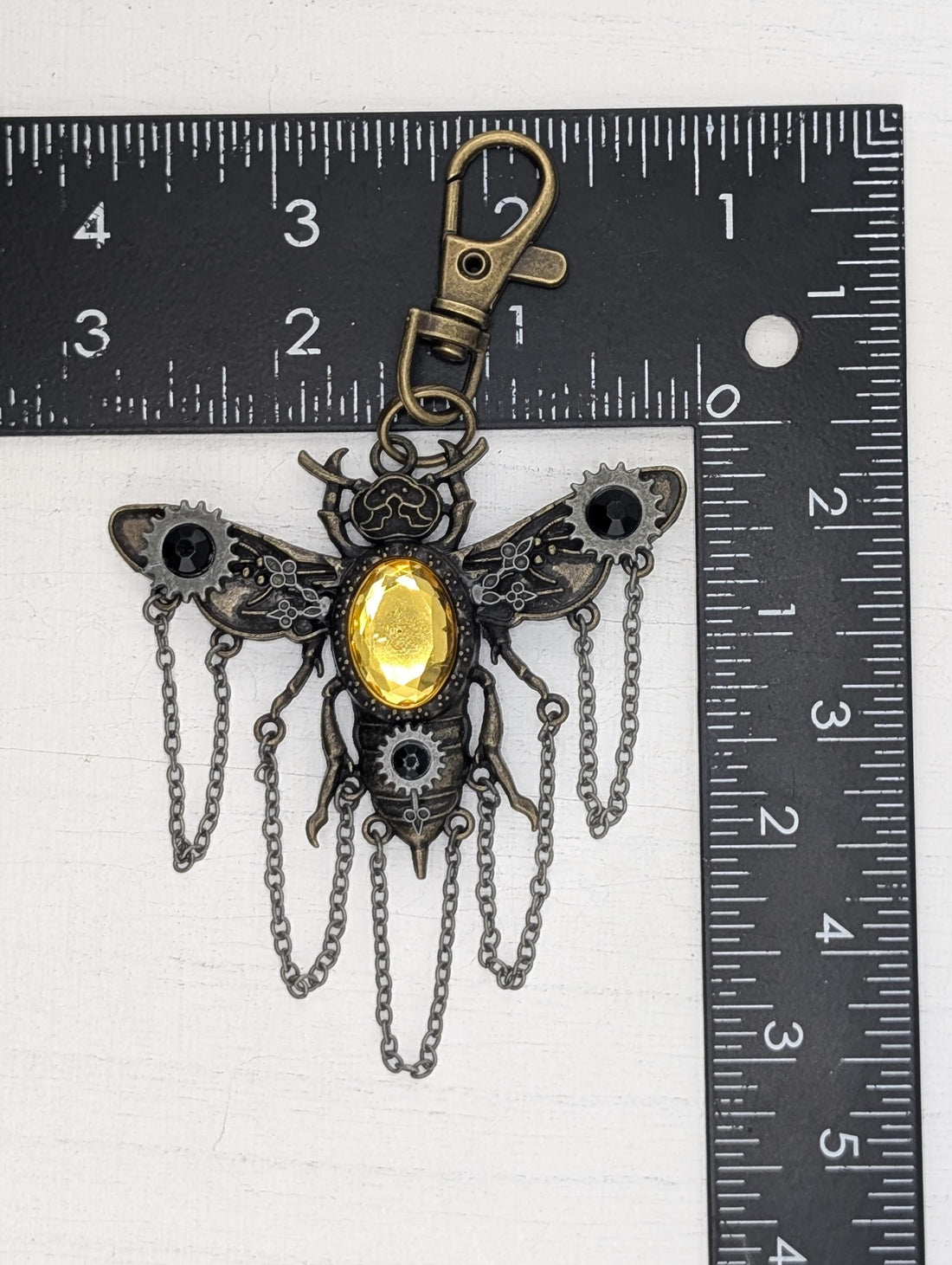 A decorative pendant in the shape of a bee, with a yellow gemstone in the center and intricate metalwork details.