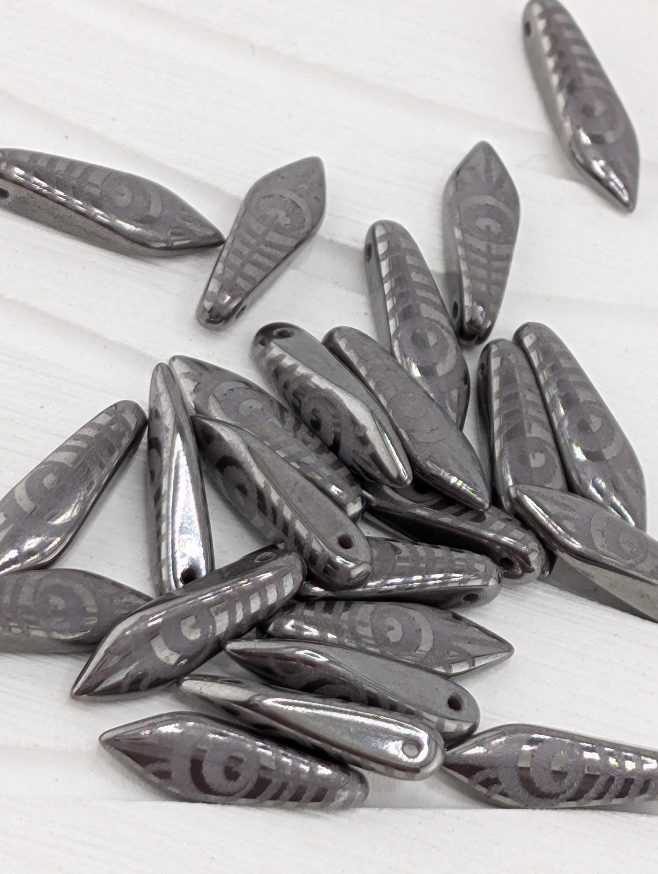 a collection of metallic beads or charms with a repeating pattern of circles or other geometric shapes, scattered on a white surface.