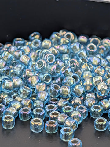 a large pile of small, clear beads in various shades of blue, scattered on a dark surface.