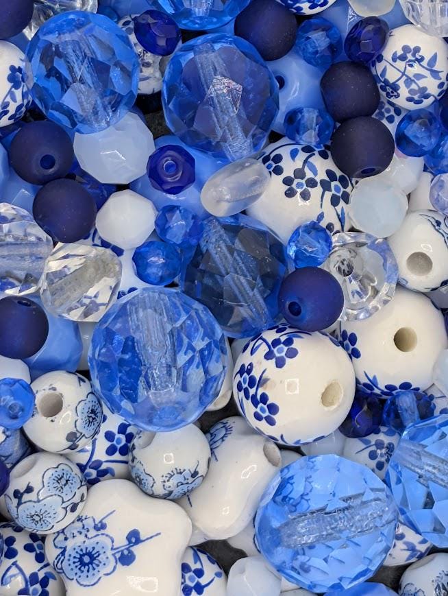 The image is a close-up of various blue and white beads, including clear and white beads, as well as blue and white beads with floral designs. The beads are scattered throughout the frame, creating a visually appealing and colorful composition.