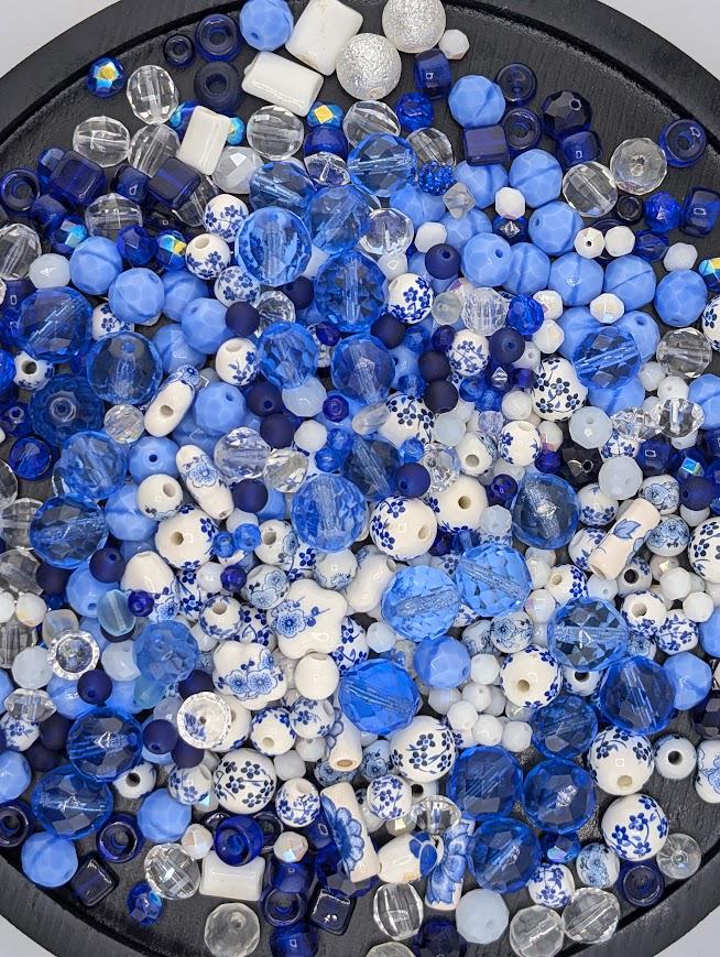 The image is a collection of various colored beads, including blue, white, and clear beads, arranged in a circular pattern.